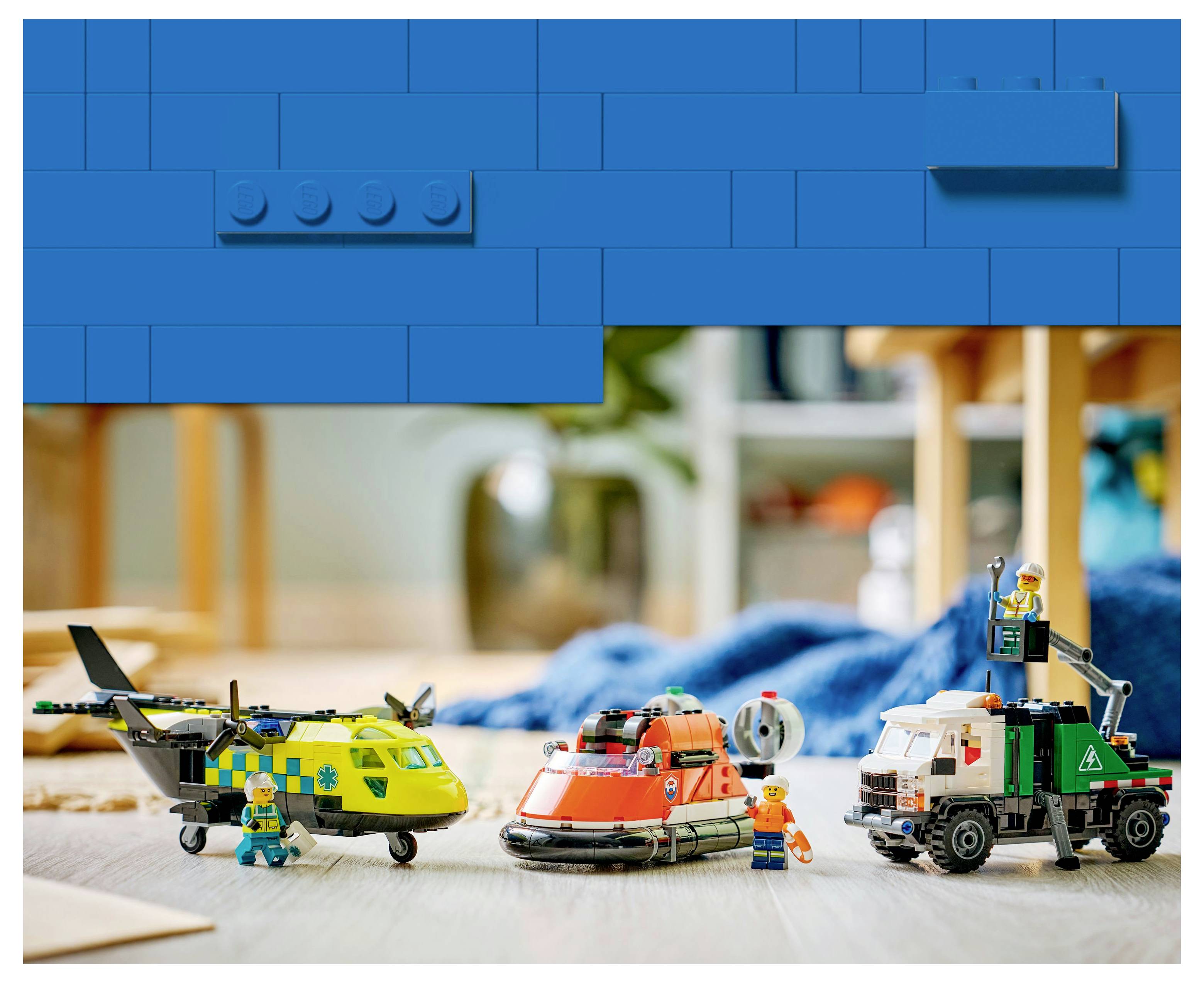 Spielzeug-Konstruktionsszene mit einem Hubschrauber, einem Hovercraft und einem Lastwagen, jeweils mit Figuren in Uniformen. Blauer LEGO-Blockrahmen oben.