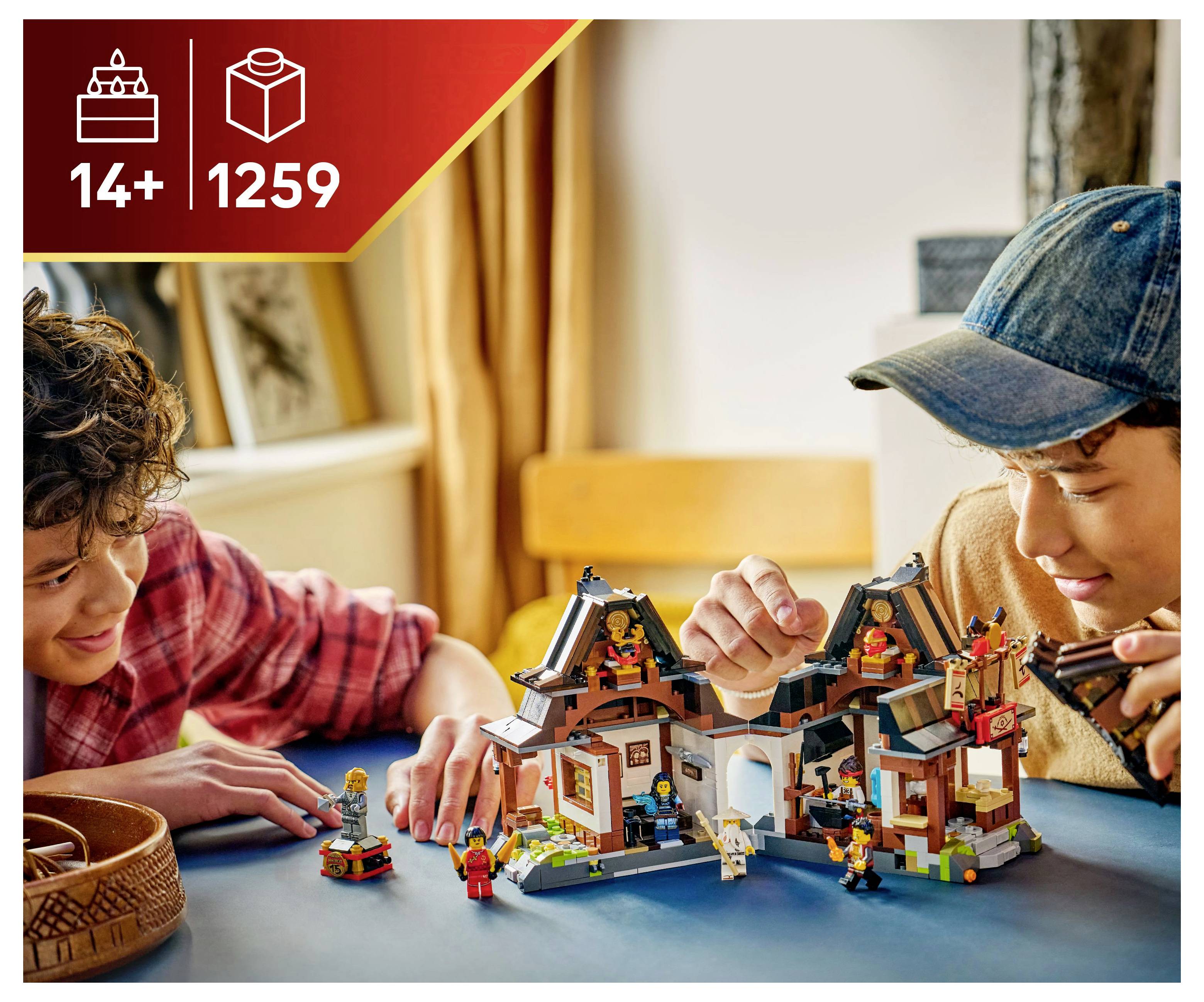 Zwei Personen bauen begeistert und spielen mit einem detaillierten LEGO-Set im asiatischen Stil auf einem blauen Tisch. Die Schachtel zeigt '14+' und '1259' Teile.