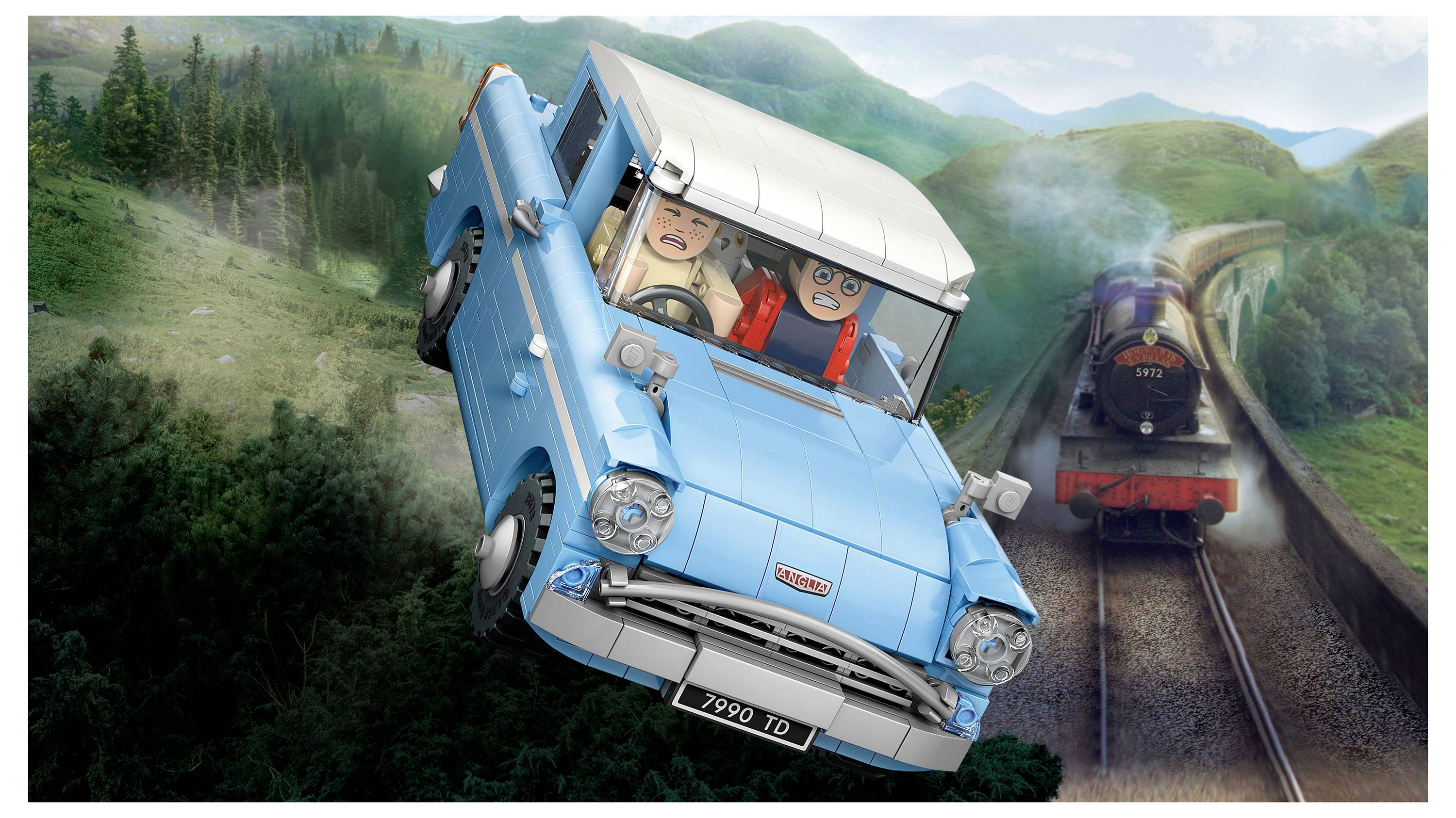 Ein blaues Spielzeugauto fliegt über eine malerische Landschaft mit zwei Figuren im Inneren; ein Zug dampft auf nahegelegenen Gleisen voran, vor einer Kulisse grüner Hügel.