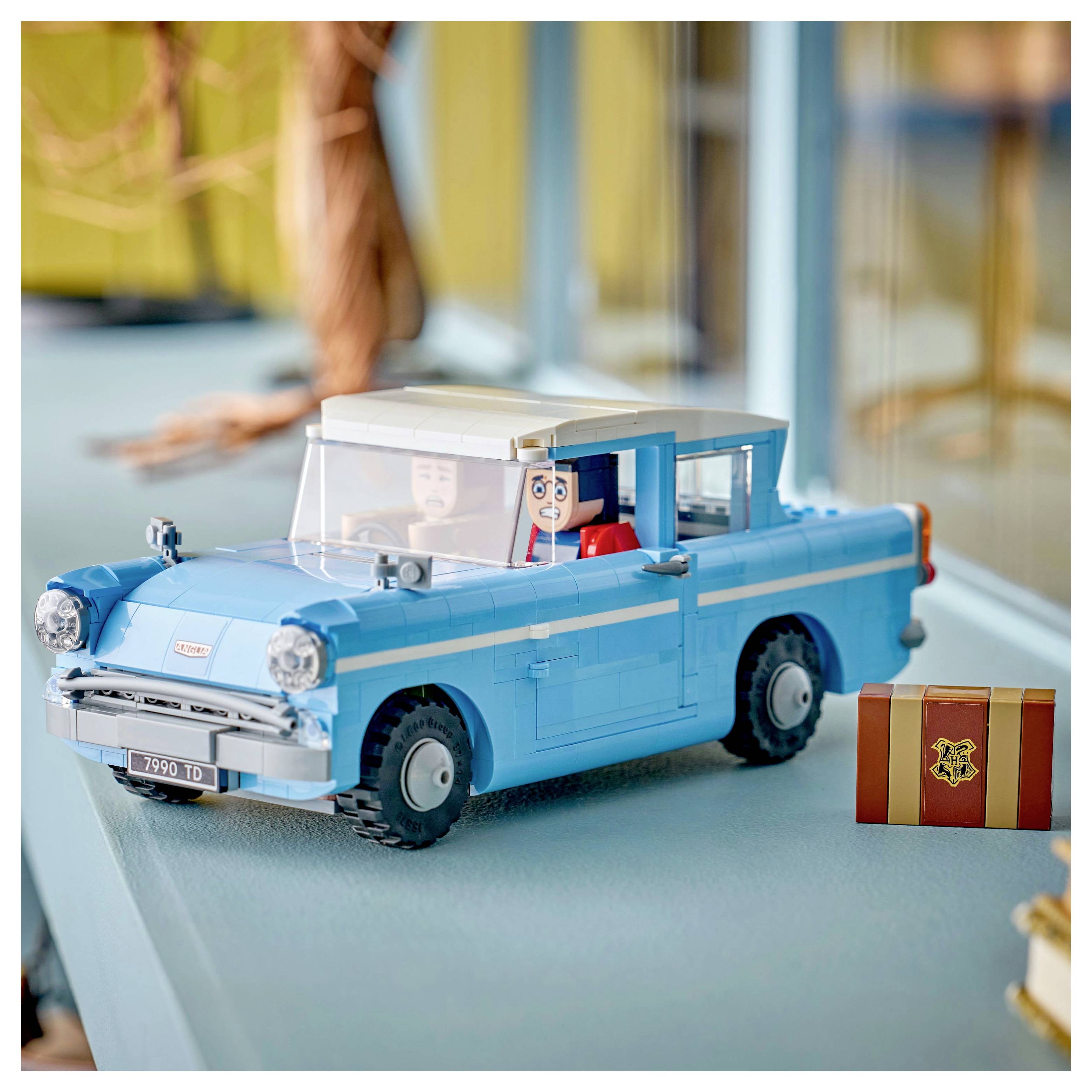 Ein Modell eines blauen Oldtimers mit Spielfiguren im Inneren, auf einem Tisch platziert, mit einer kleinen braunen und goldenen Box in der Nähe.