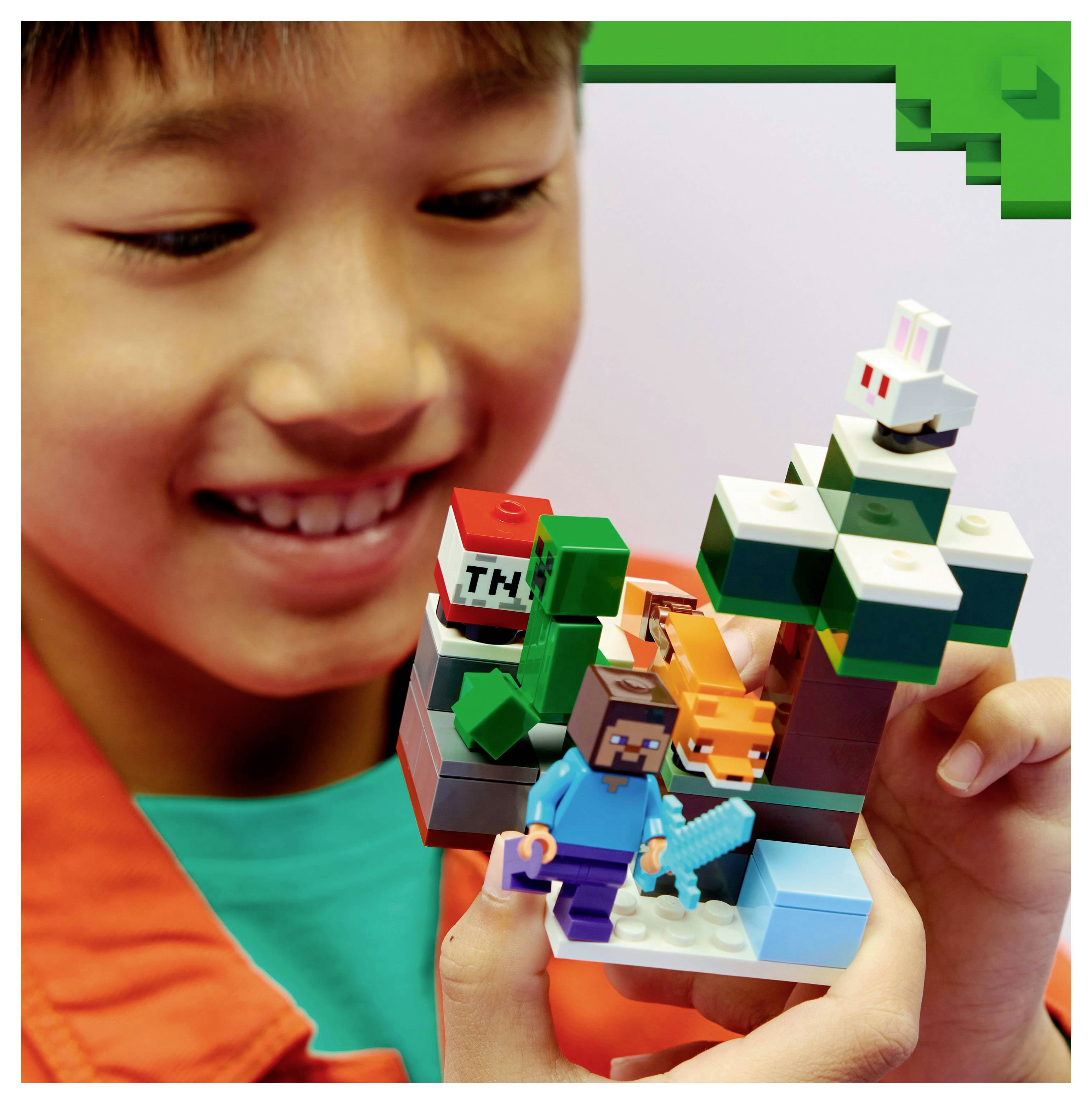 Ein Kind, das ein LEGO Minecraft-Set hält, das ikonische Charaktere und Elemente wie einen Baum, einen Fuchs, einen Creeper und einen TNT-Block zeigt, lächelt voller Aufregung.
