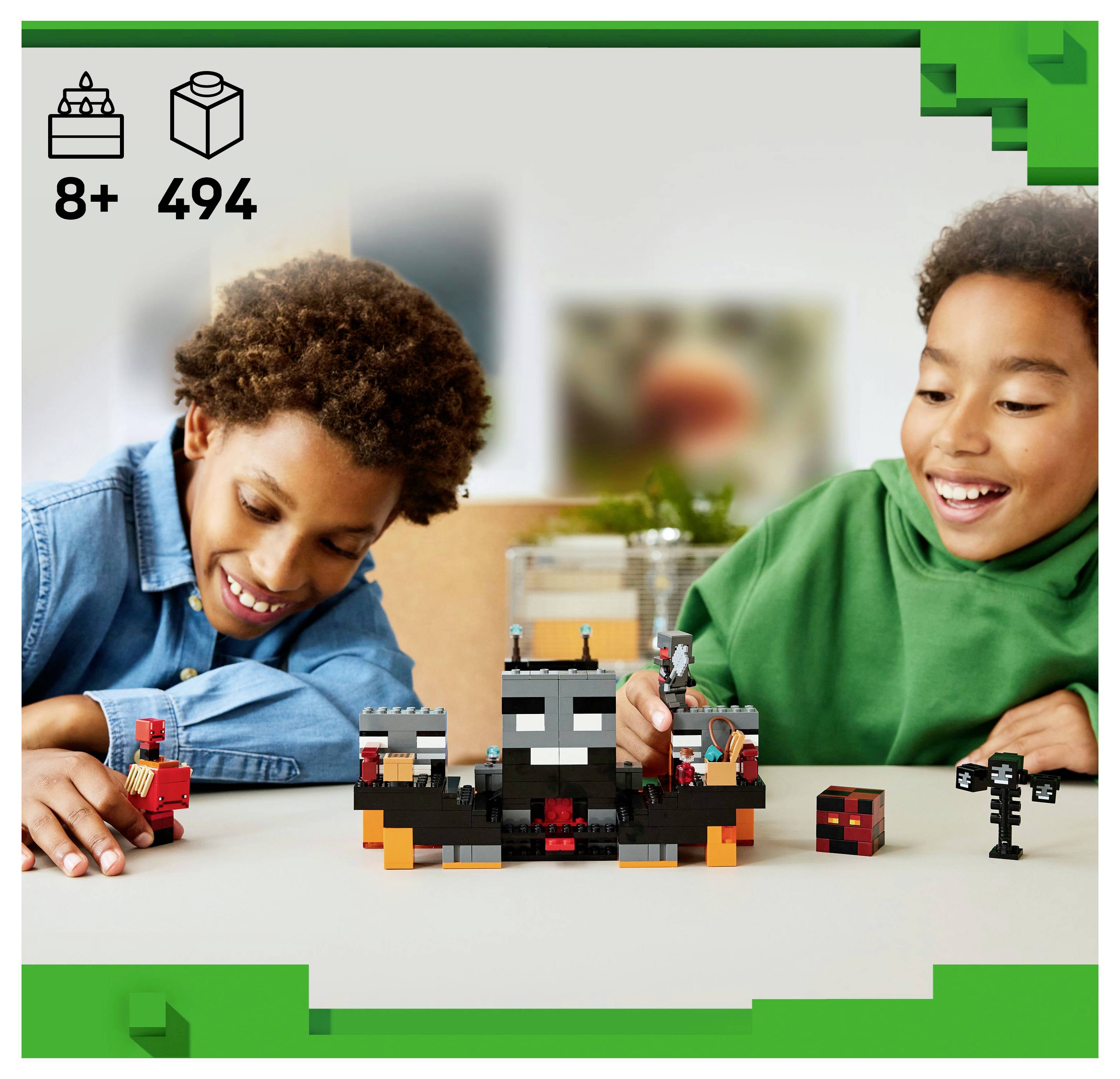 Zwei Kinder lächeln, während sie mit einem Minecraft-Themen-LEGO-Set spielen, das eine eckige Kreatur zeigt, vor einem neutralen Innenraum-Hintergrund.