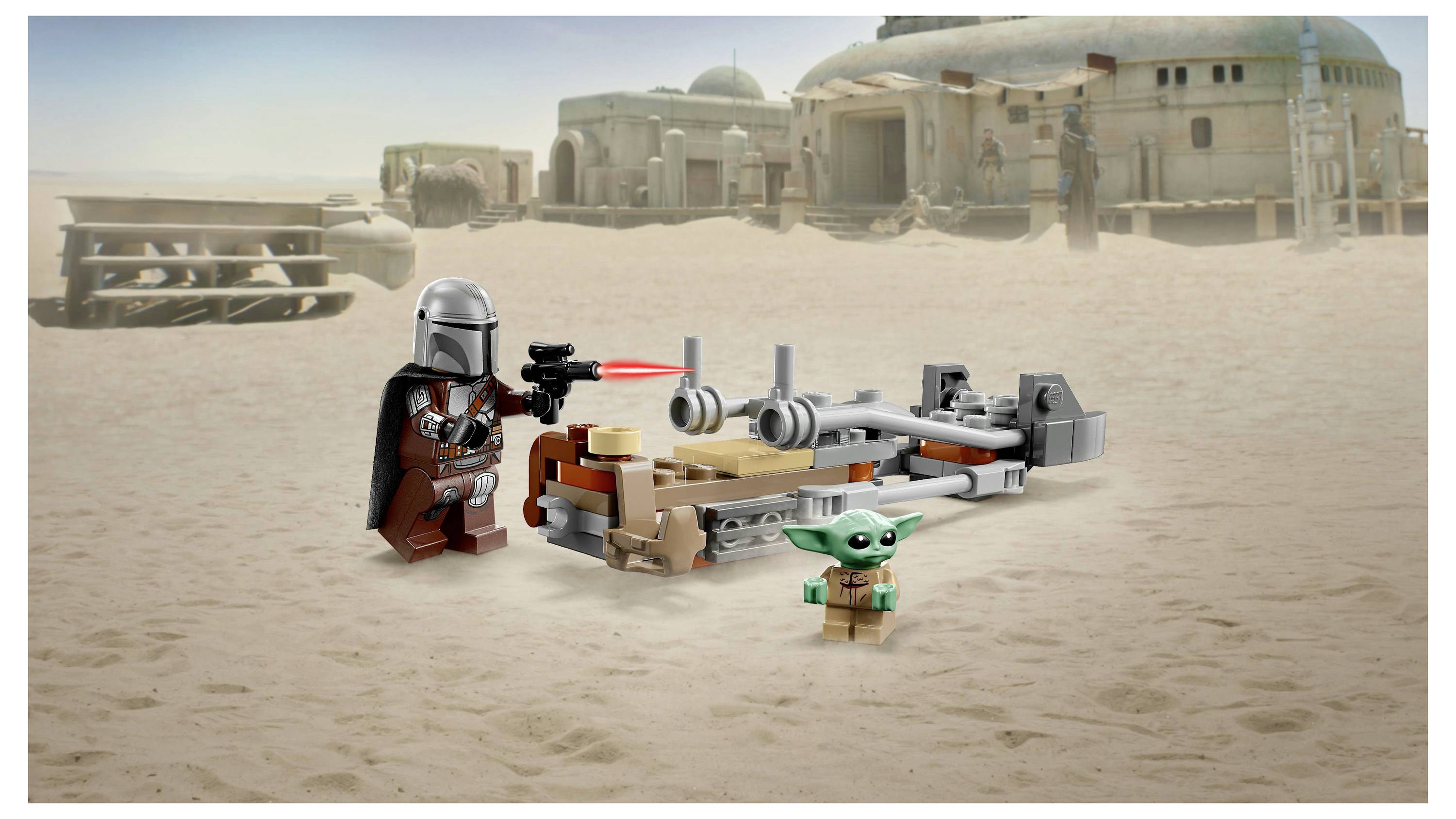 Lego-Figuren eines Charakters mit Helm und einer kleinen grünen Kreatur stehen neben einem Raumschiff in einer Wüste mit einem Gebäude im Hintergrund.