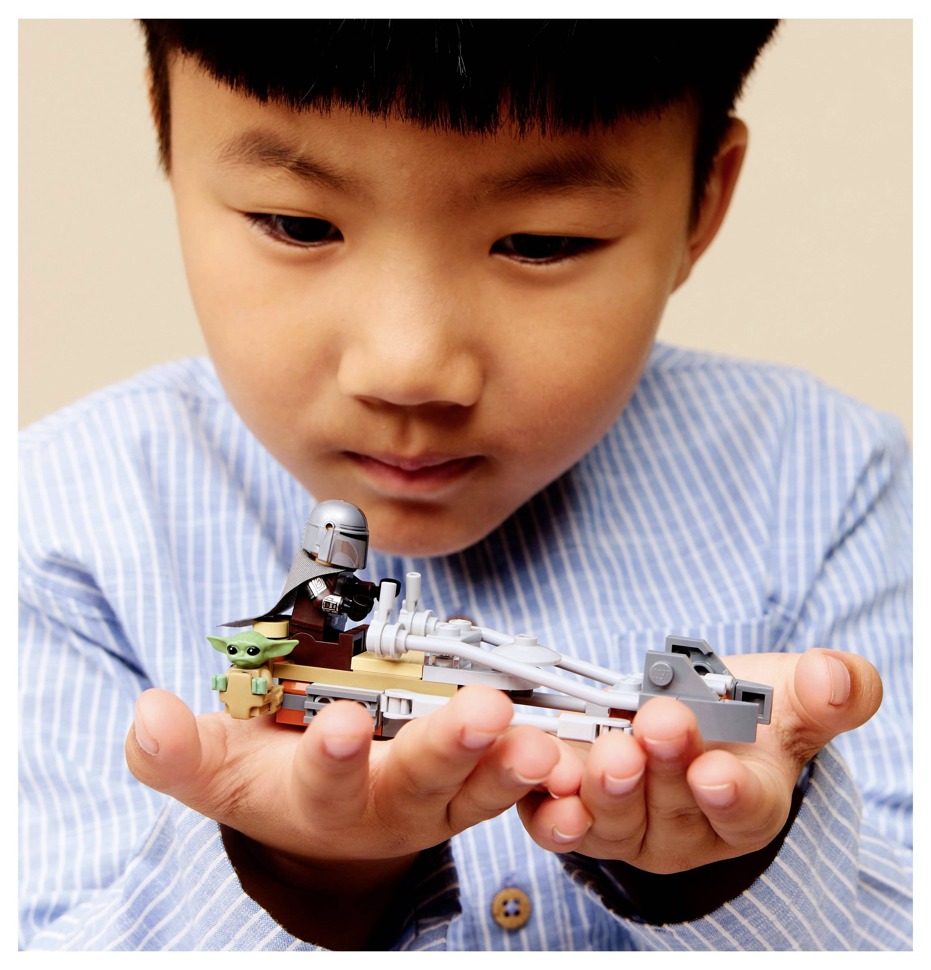 Ein Kind hält ein LEGO-Set mit einer kleinen Figur in Rüstung und einer grünen Figur, die beide Charakteren aus einer beliebten Science-Fiction-Serie ähneln.