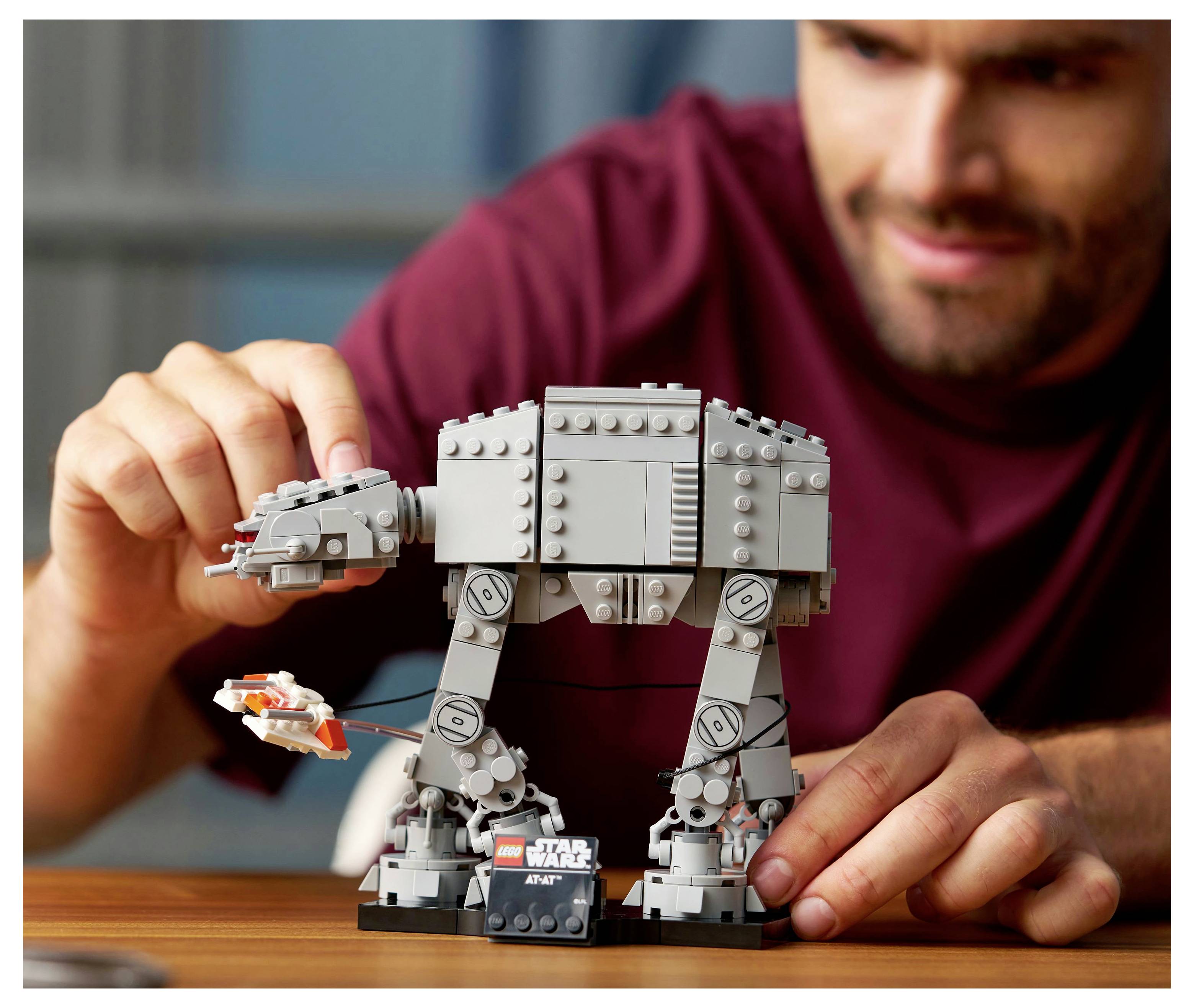 Eine Person montiert ein LEGO 'Star Wars AT-AT' Modell mit beweglichen Beinen und einem kleinen Raumschiff, was auf eine Szenengestaltungsaktivität hindeutet.