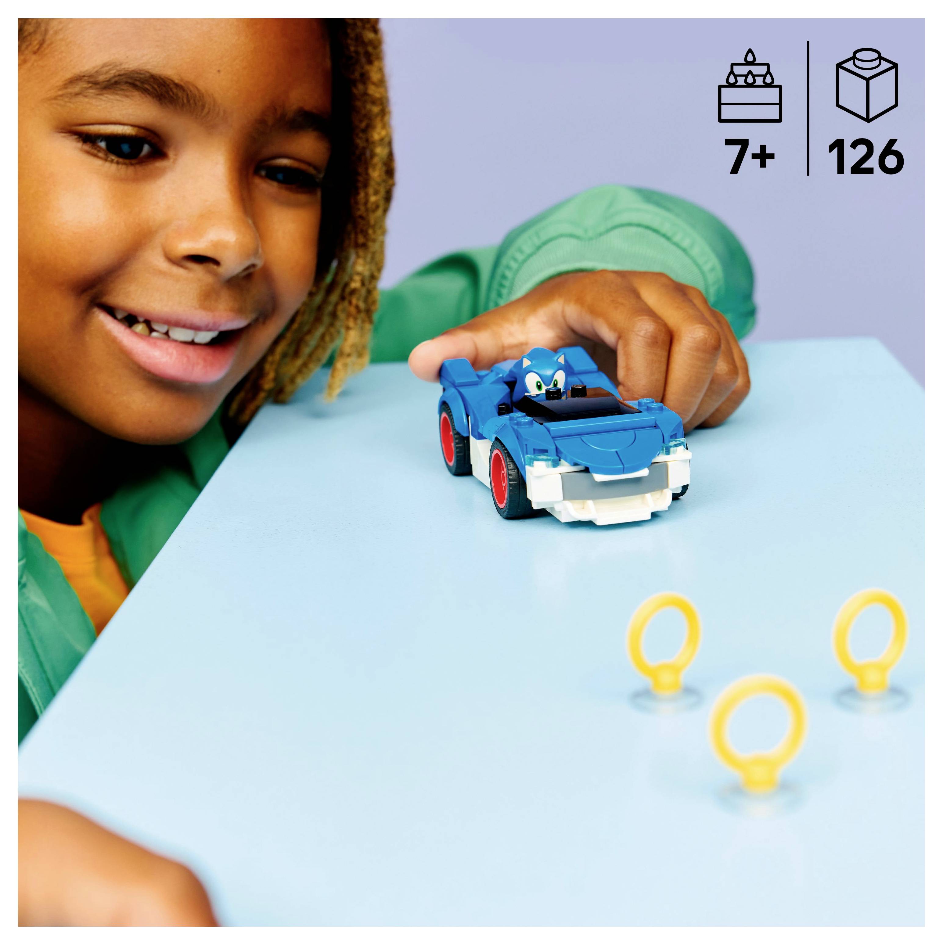 Ein Kind, das mit einem blauen Spielzeugauto mit einer Figur spielt, umgeben von kleinen gelben Ringen. Das Bild zeigt die Eignung für Kinder ab 7 Jahren und enthält 126 Teile.