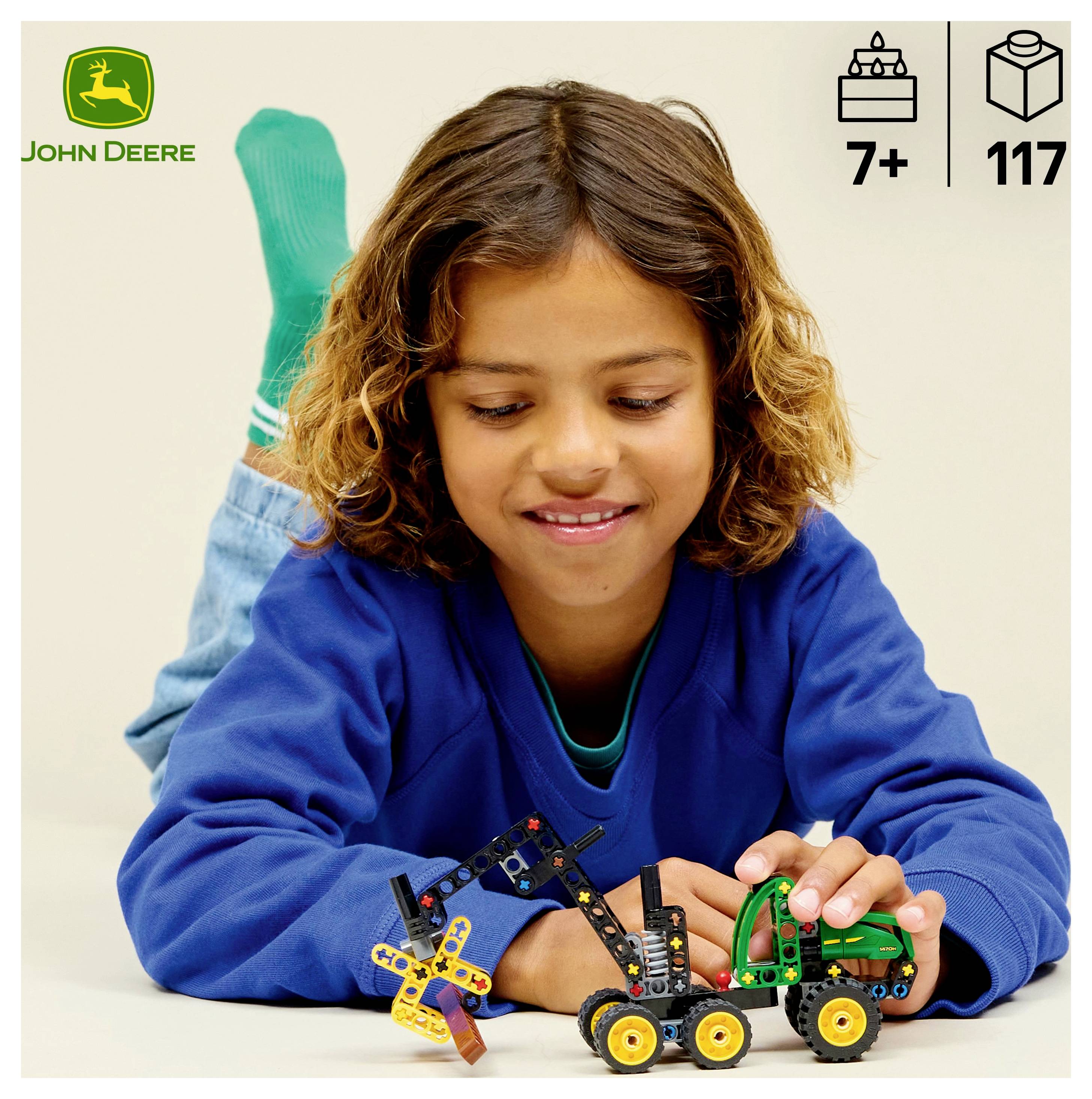 Ein Kind in einem blauen Pullover spielt mit einem John Deere Spielzeugtraktor. Symbole zeigen an, dass es für Kinder ab 7 Jahren geeignet ist und 117 Teile enthält.