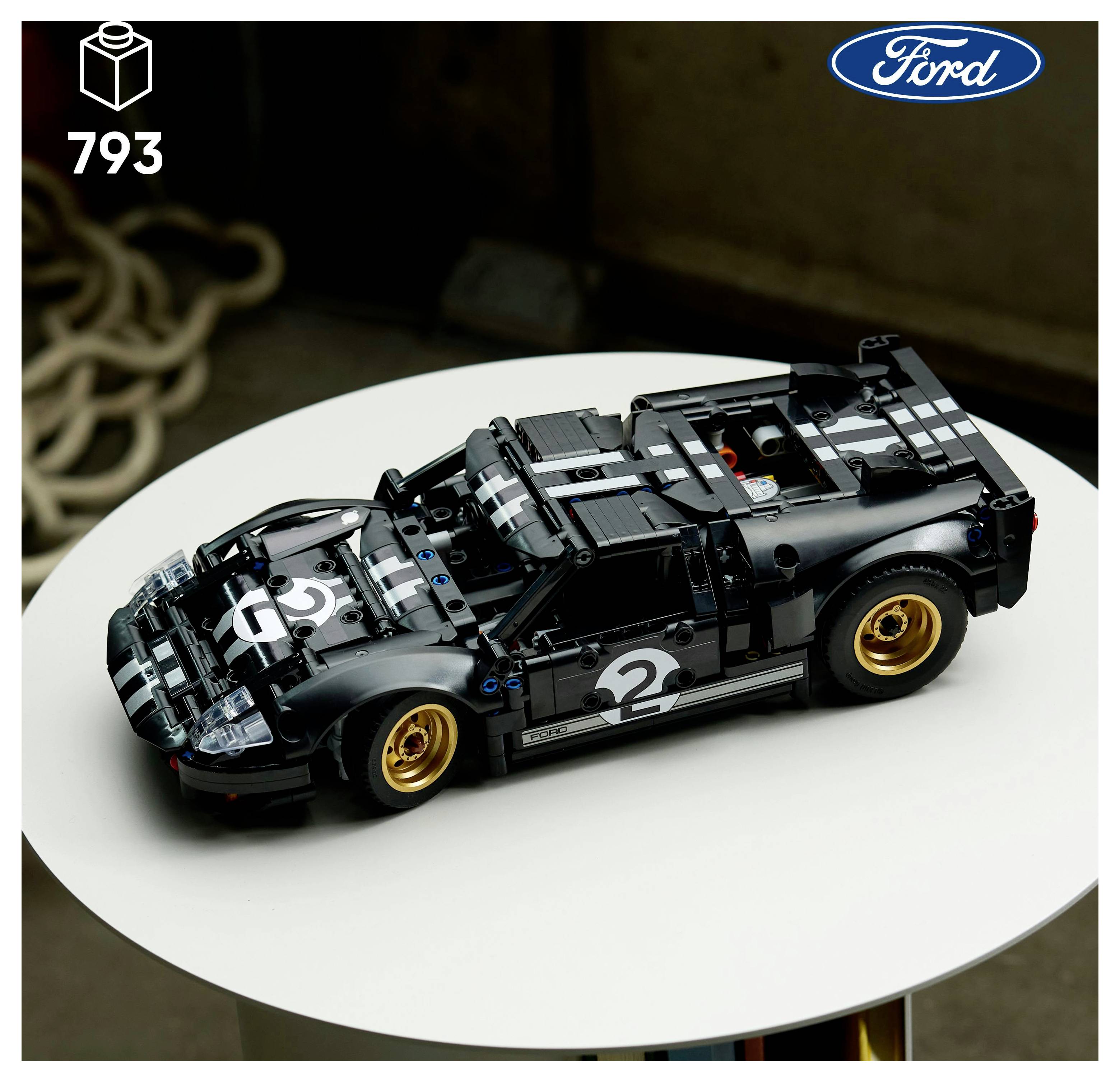 Ein schwarzes LEGO Ford GT Modell mit Rennstreifen und goldenen Felgen auf einem runden weißen Tisch. Das Ford-Logo befindet sich in der oberen rechten Ecke.