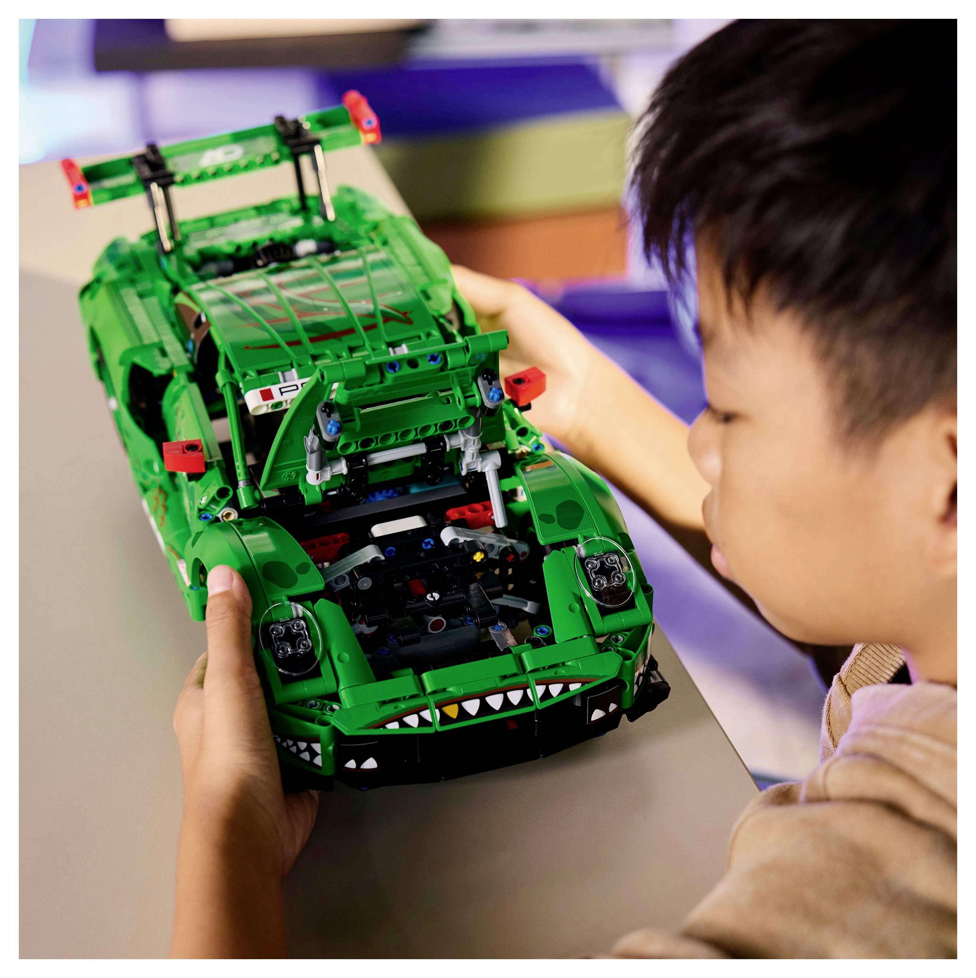 Ein Kind setzt ein grünes Spielzeugauto mit kunstvollen Details auf einem Tisch zusammen und konzentriert sich darauf, die Einzelteile präzise zu platzieren.