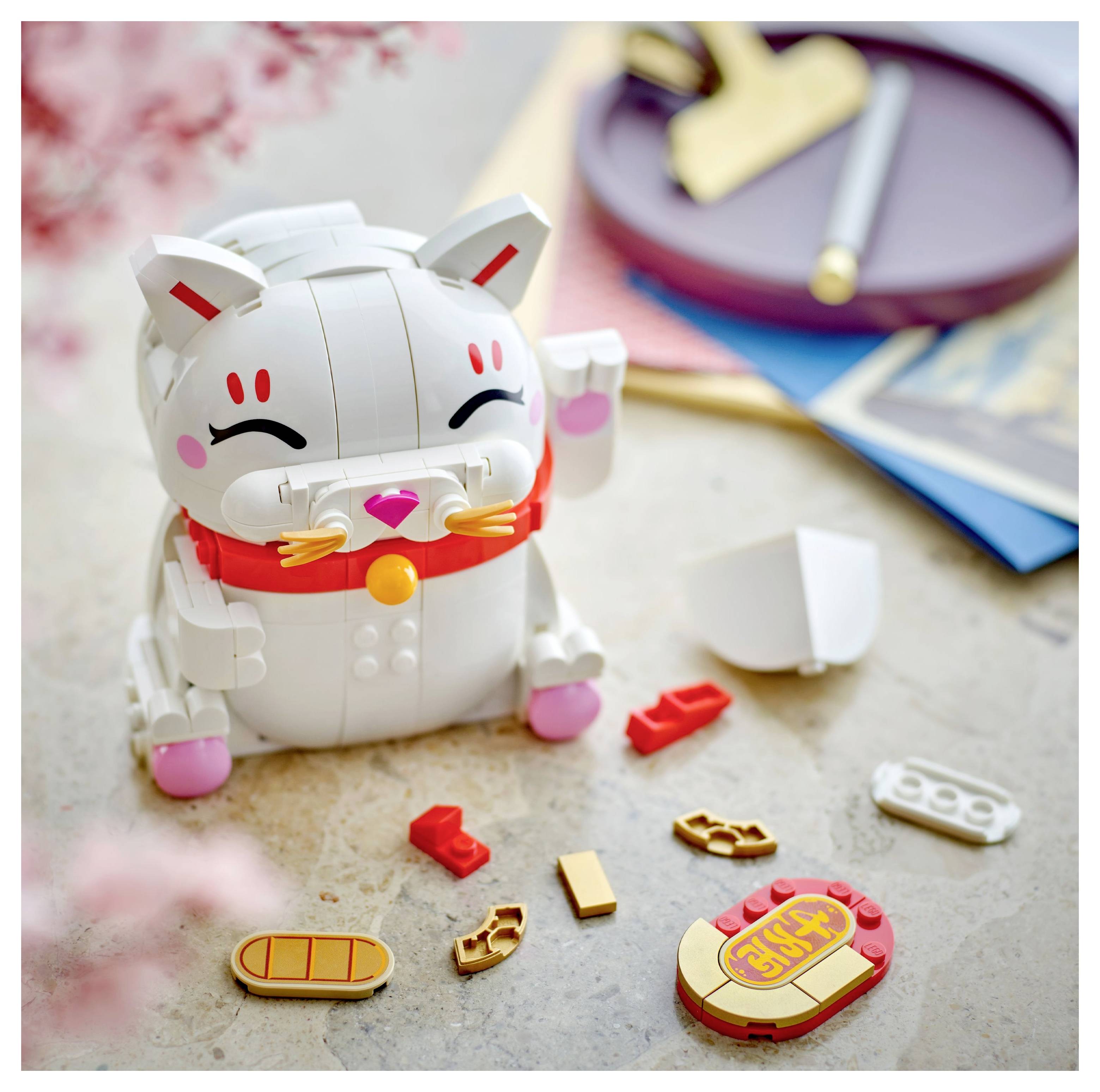 Ein Spielzeugkatzen-Bausatz mit einer lächelnden weißen Katze mit roten Markierungen und verschiedenen verstreuten Teilen, einschließlich Pfoten und einer Glocke.