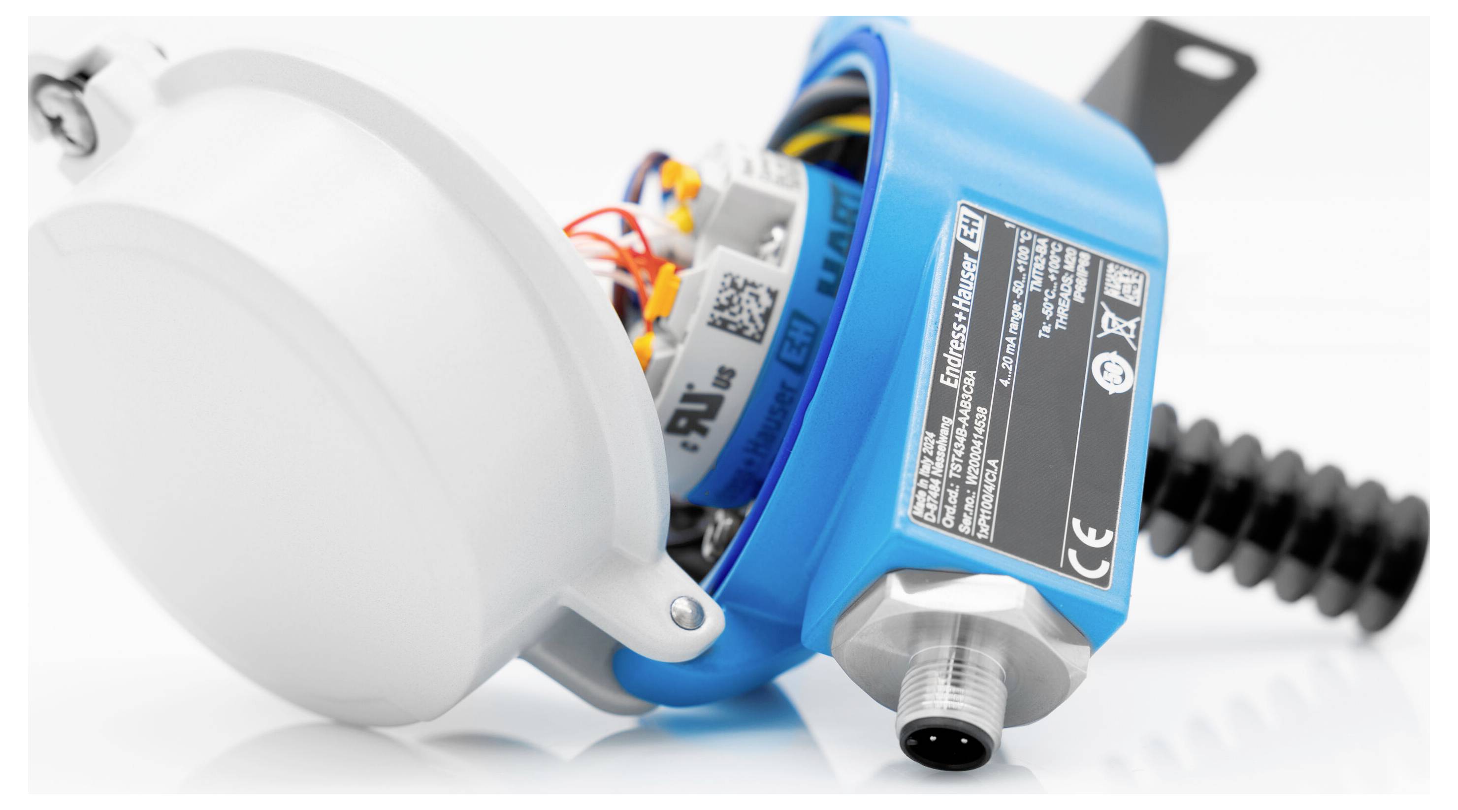 Nahaufnahme eines blauen Industrie-Sensors oder Steuergeräts mit offener weißer Abdeckung, die interne Verkabelung und eine schwarze Kabelverbindung zeigt.