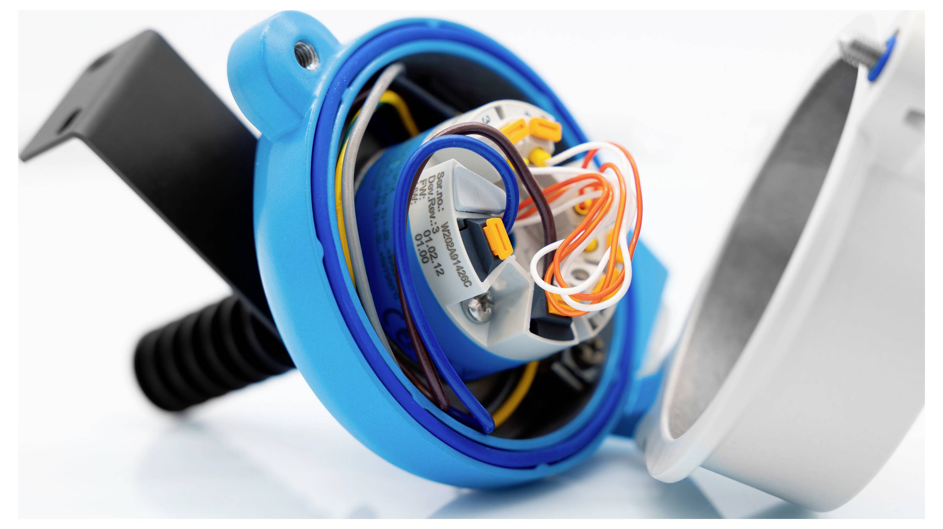 Blauer elektrischer Sensor oder Schalter auf einem Metallpanel montiert neben einem aufgerollten Kabel und unscharfem Gemüse im Vordergrund