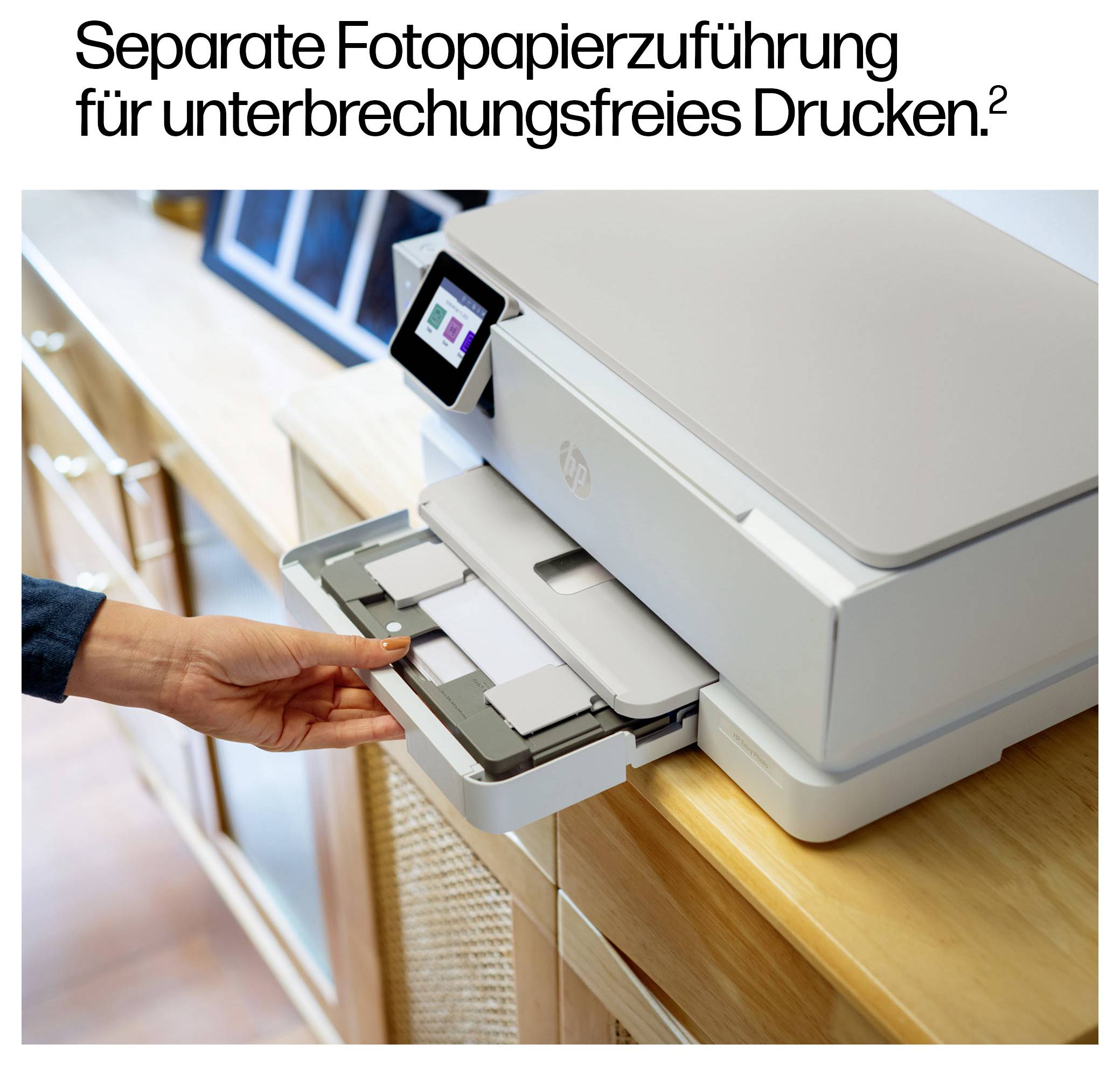 Eine Person legt Fotopapier in ein Papierfach auf einem Holztresen. Der Drucker verfügt über ein digitales Display. Text oben lautet: 'Separate Fotopapierzuführung für unterbrechungsfreies Drucken'.