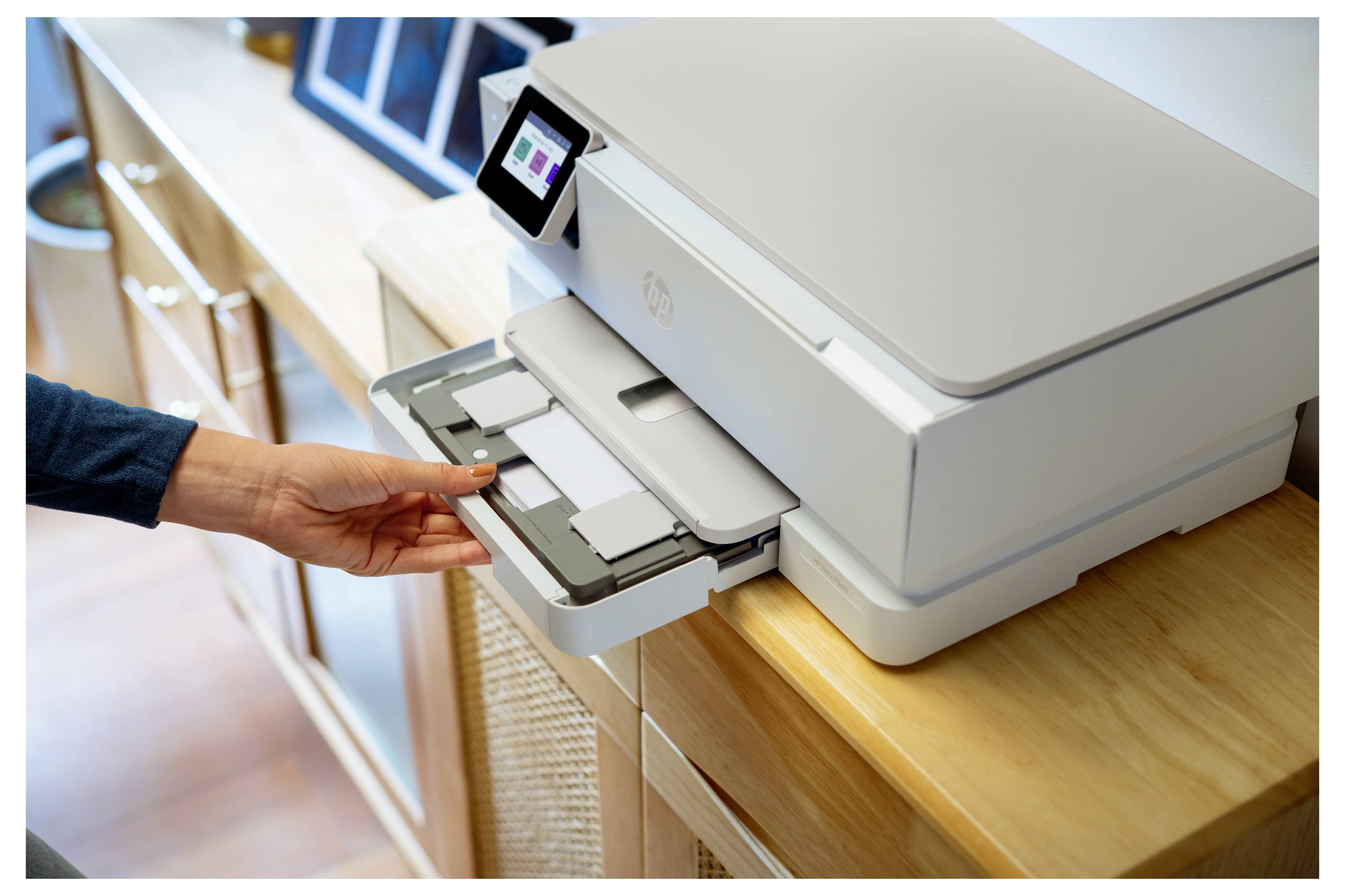 Eine Person legt ein Dokument in den Papierschacht eines weißen Druckers in einem hell erleuchteten Raum. Der Drucker verfügt über ein kleines digitales Display.