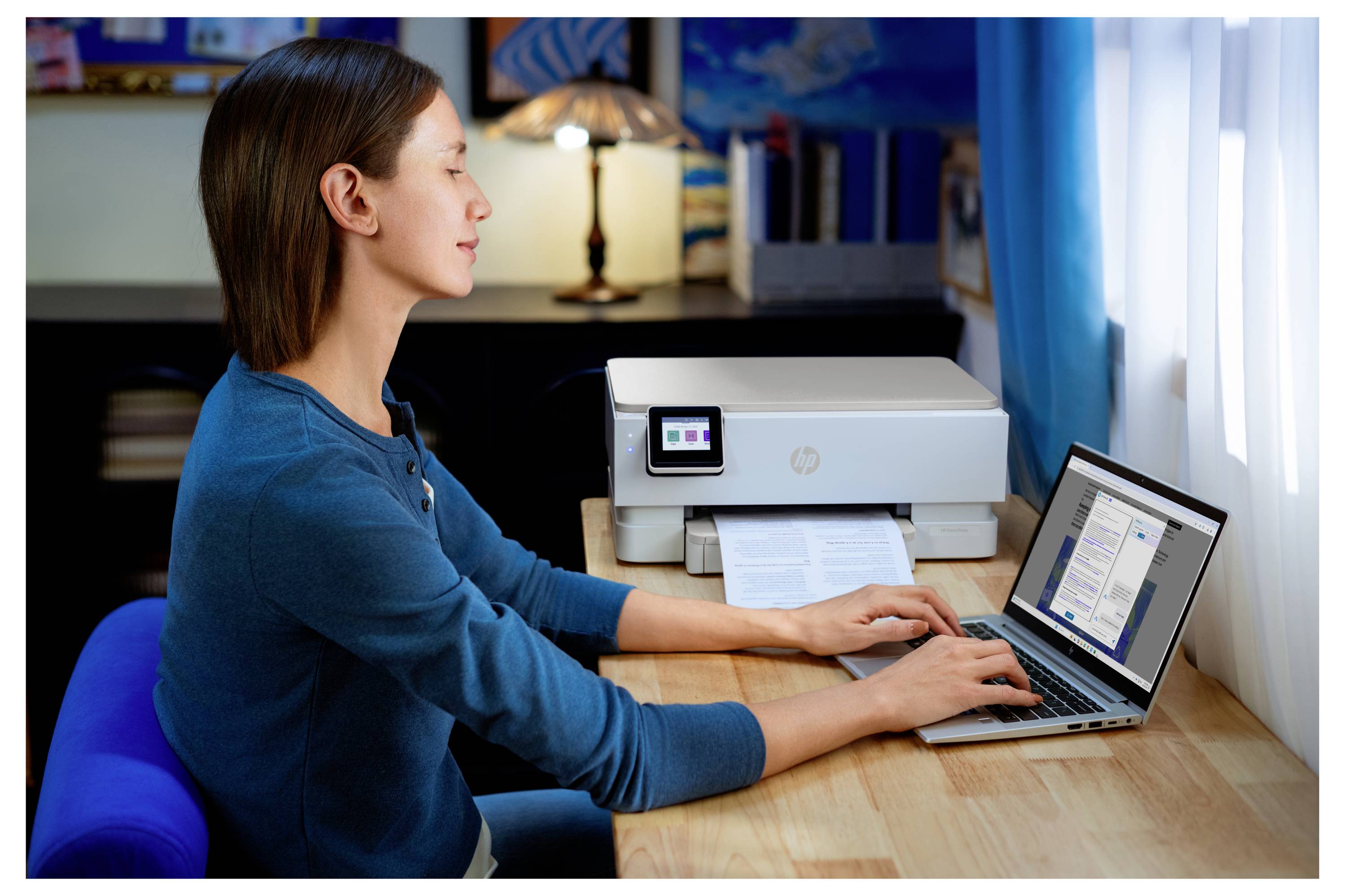 Eine Person, die einen Laptop neben einem Drucker auf einem Schreibtisch in einem Heimarbeitszimmer benutzt, was auf einen laufenden Druckauftrag hindeutet.