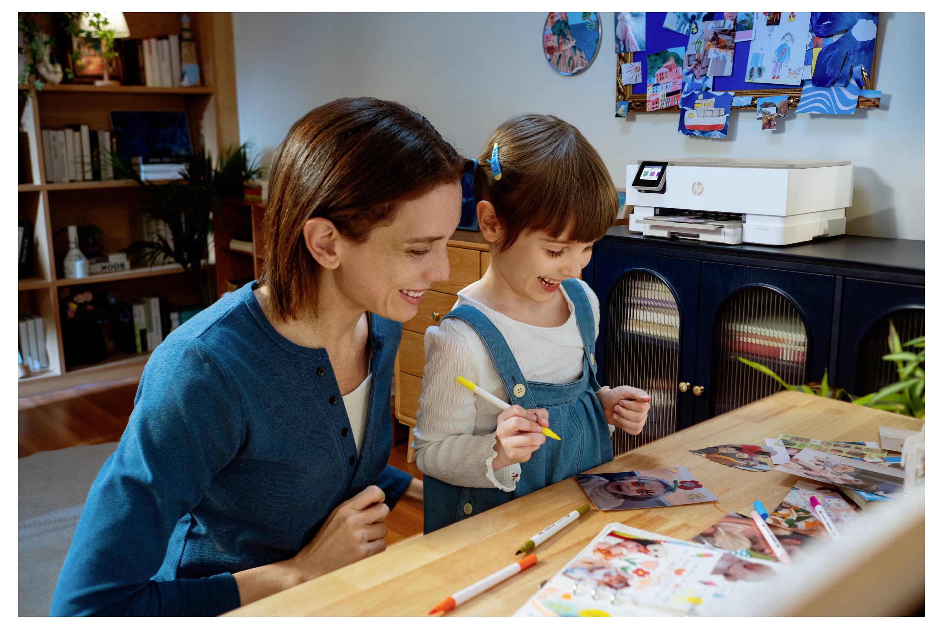 Eine Mutter und Tochter basteln gemeinsam fröhlich an einem Holztisch, umgeben von Bastelmaterialien und Fotos in einem gemütlichen, mit Büchern gefüllten Raum.