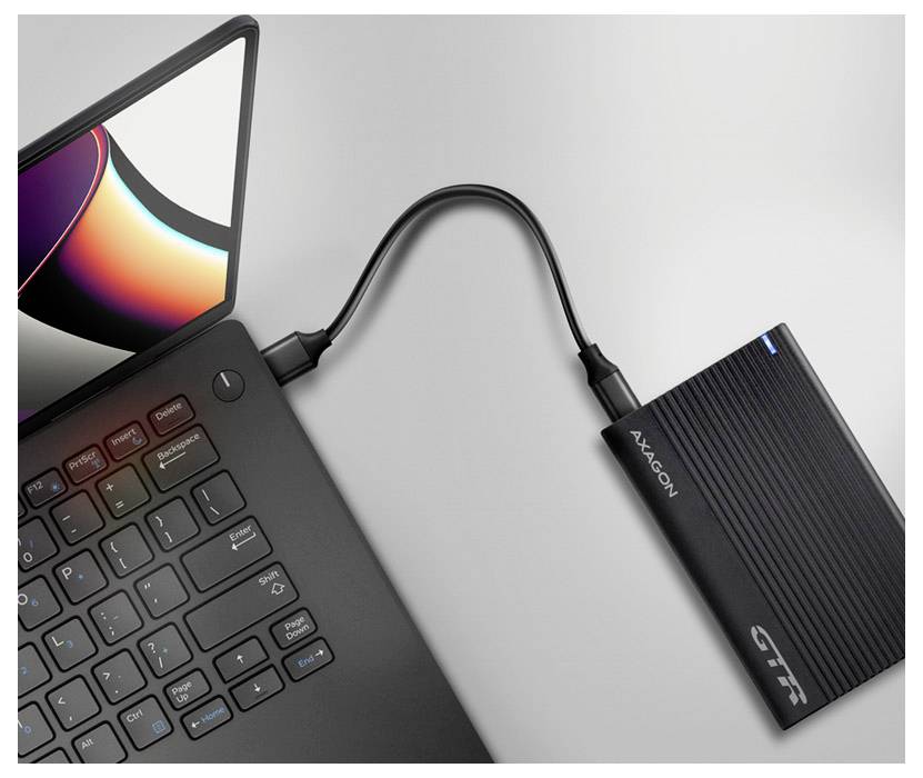Eine Nahaufnahme eines Laptops mit schwarzer Tastatur, der über ein kurzes USB-Kabel mit einer tragbaren externen Festplatte verbunden ist.