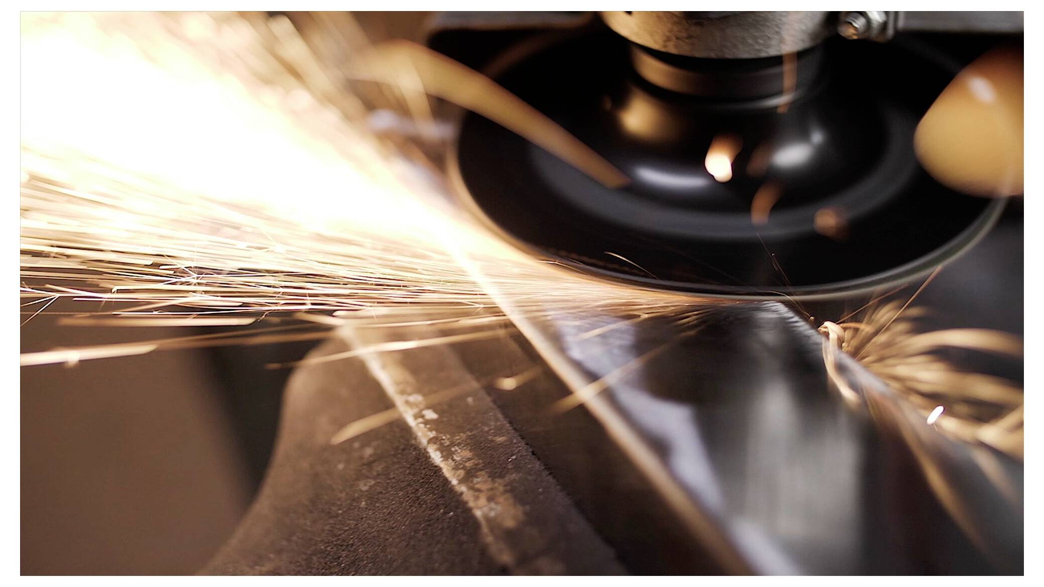 Eine Nahaufnahme einer rotierenden Winkelschleifmaschine, die beim Glätten einer Metalloberfläche helle Funken ausstößt.