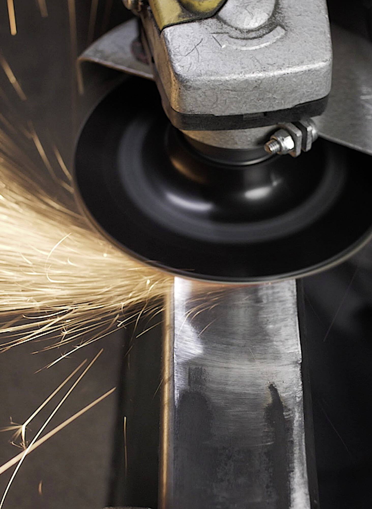 Eine Metallschleifmaschine schneidet einen Stahlträger und erzeugt dabei helle orange Funken, die von der Kontaktstelle nach außen sprühen.