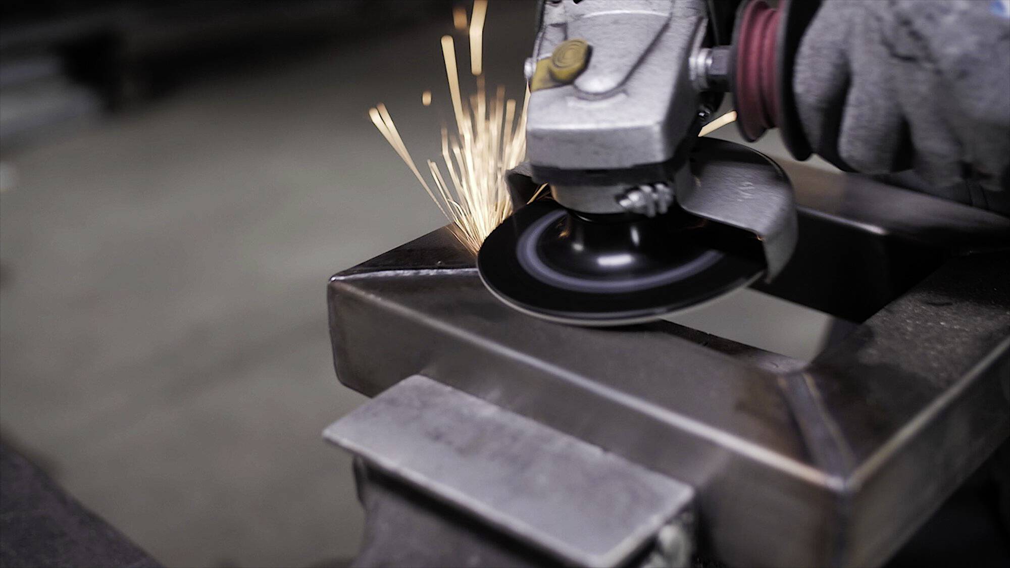 Eine Nahaufnahme einer Person, die eine tragbare Winkelschleifer verwendet, um Metallkanten zu glätten, wobei Funken sprühen. Die Person trägt Schutzhandschuhe.