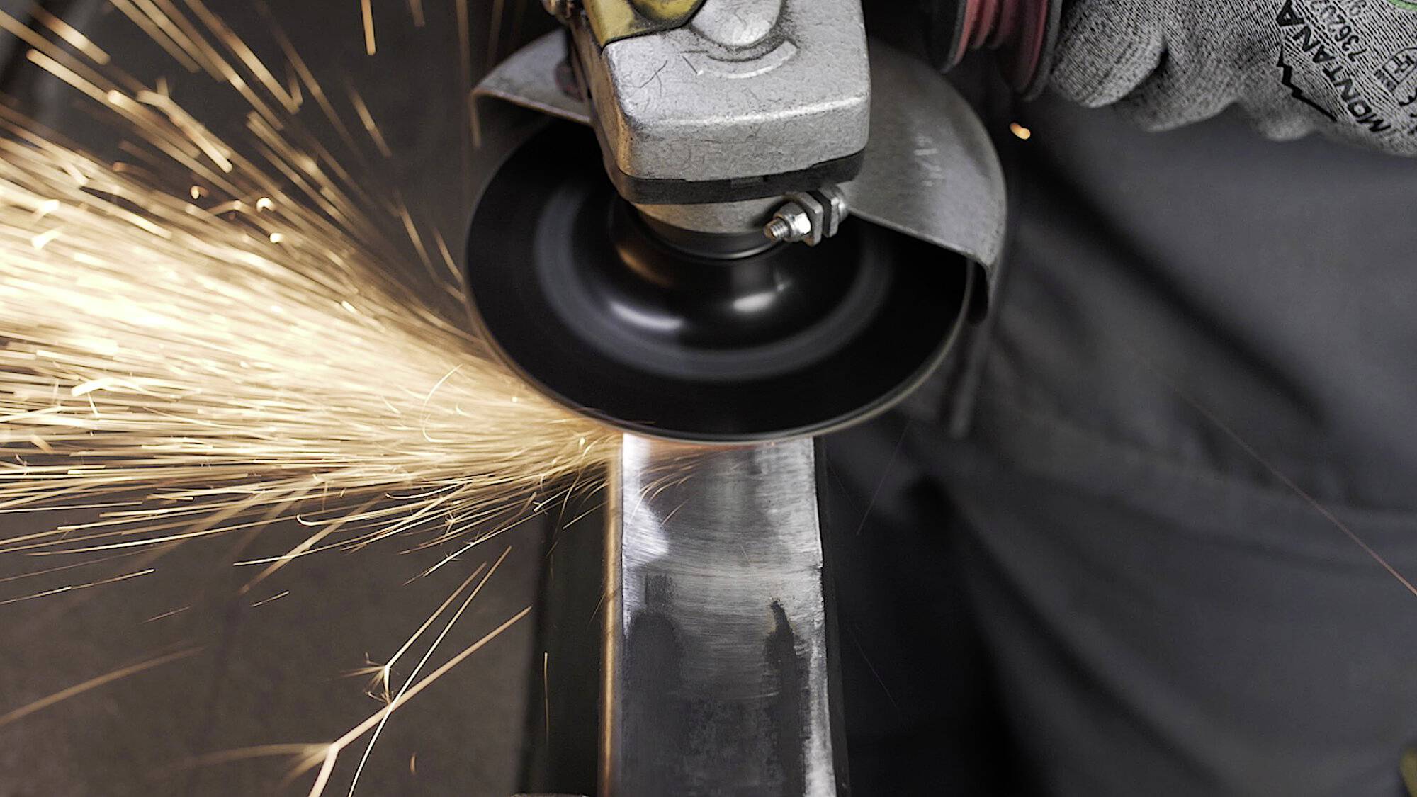 Eine Person mit Handschuhen verwendet eine Winkelschleifer, um Metall zu schneiden oder zu polieren und erzeugt dabei helle, sich bewegende Funken.