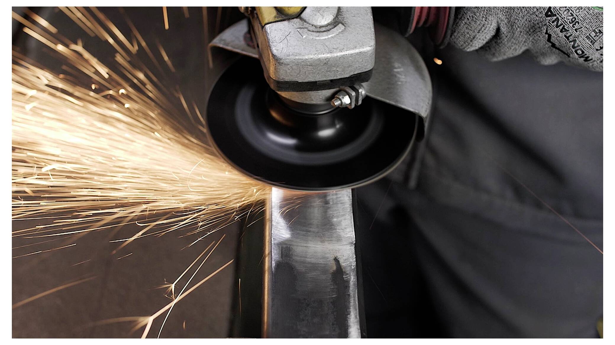 Ein Arbeiter verwendet einen Winkelschleifer und erzeugt dabei helle Funken, während er Metall schneidet. Der Arbeiter trägt Schutzhandschuhe und gewährleistet so die Sicherheit bei der Aufgabe.