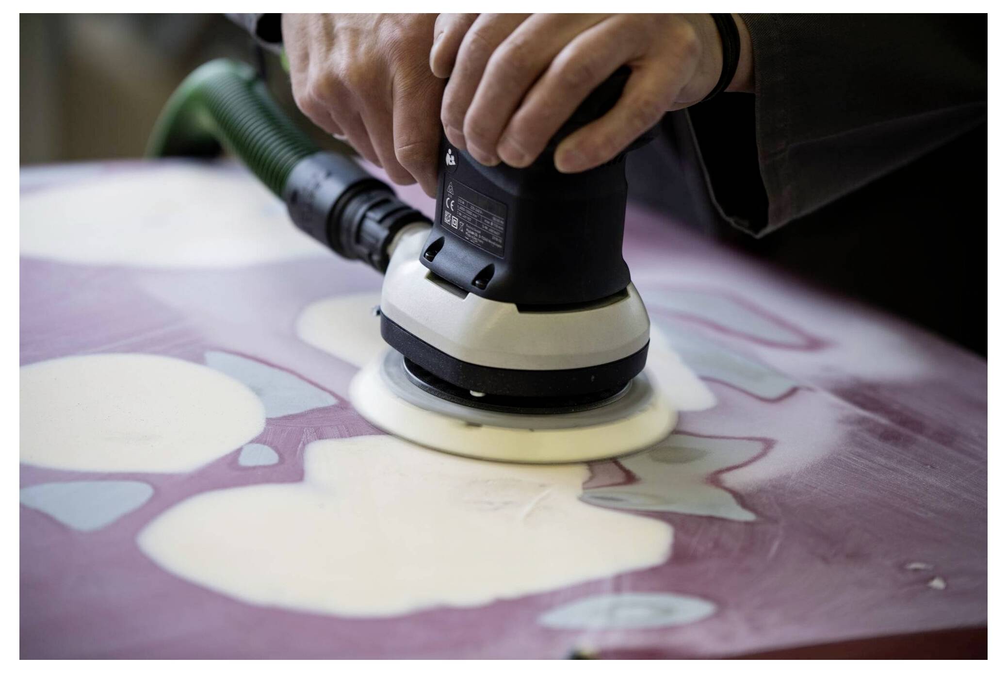 Eine Person verwendet eine elektrische Schleifmaschine, um eine Holzoberfläche mit weißen und rosa Flecken zu glätten und legt dabei Wert auf Detailarbeit.