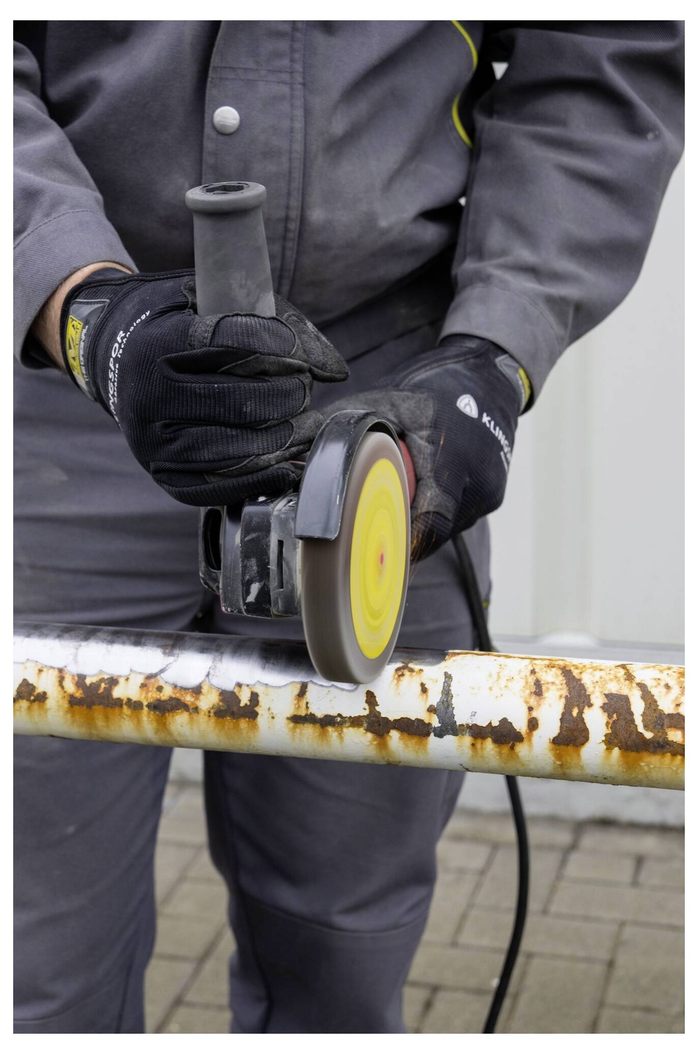 Eine Person mit Handschuhen entfernt mit einer Winkelschleifmaschine Rost von einem Metallrohr und bereitet es für das Neustreichen oder Wartungsarbeiten vor.