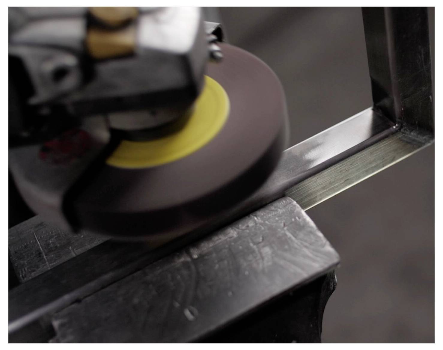 Eine Nahaufnahme einer Schleifmaschine, die die Kanten eines Metallstücks glättet, wobei Funken sprühen. Die Maschine ist in Bewegung und konzentriert sich auf Effizienz.