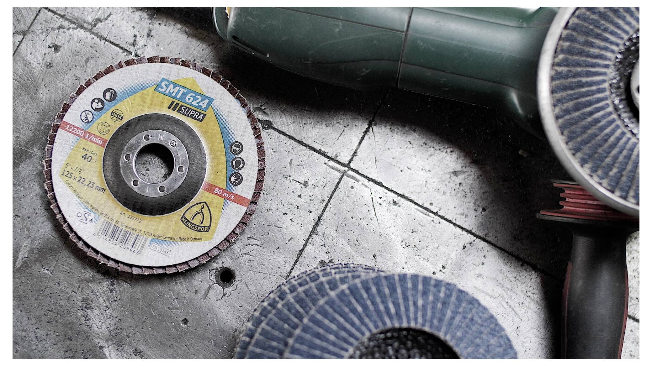 Nahaufnahme einer Schleiflamellenscheibe und eines Winkelschleifers auf einer Betonoberfläche, was auf laufende Bau- oder Reparaturarbeiten hindeutet.