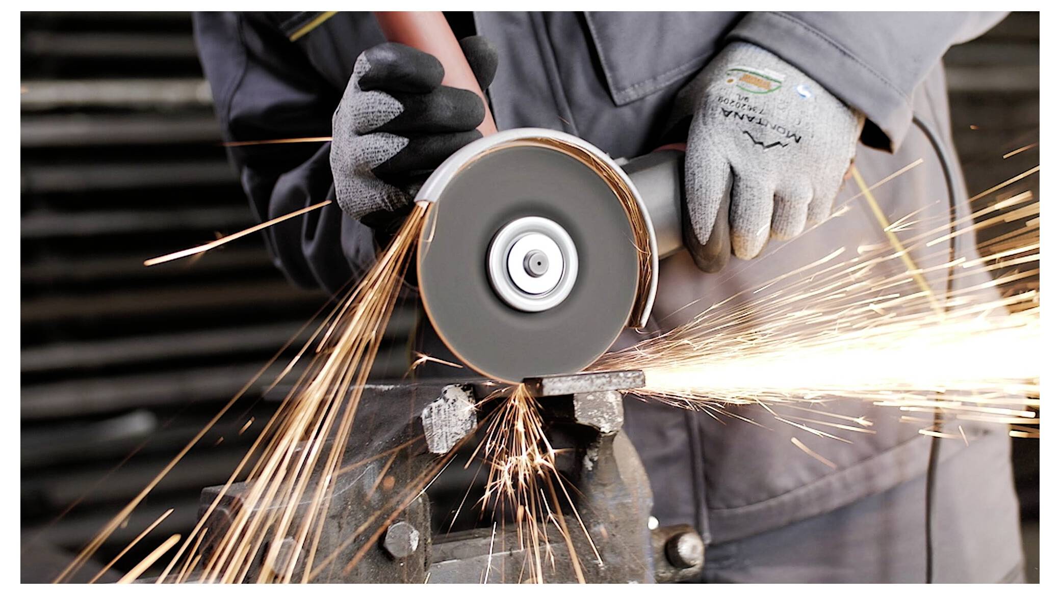 Eine Person mit Handschuhen bedient eine Winkelschleifer und erzeugt dabei helle Funken. Der Fokus liegt auf dem Werkzeug und der Bewegung des Metallschnitts.
