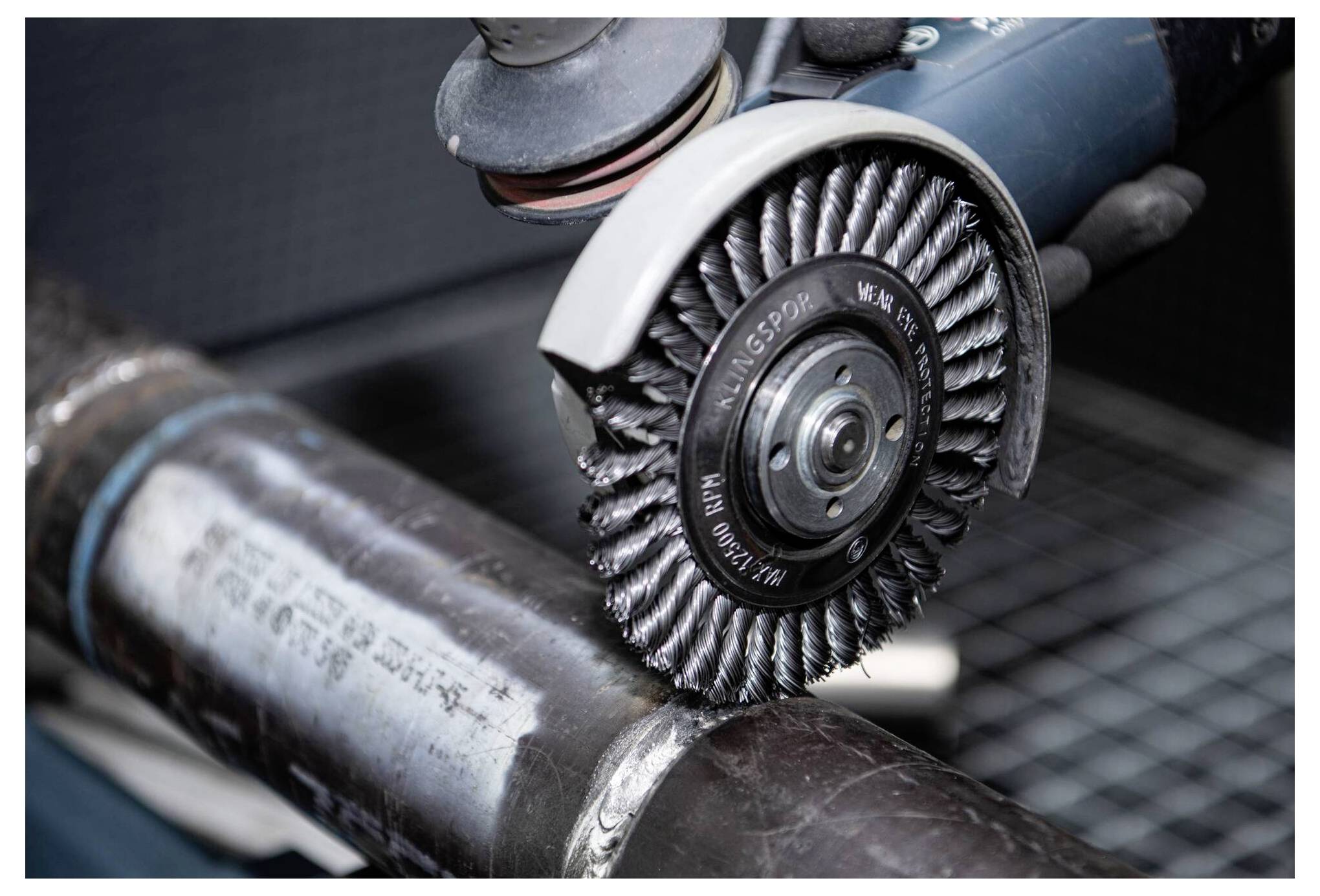 Eine Elektrowerkzeug mit Drahtbürsten-Aufsatz poliert eine Metallröhre und glättet die Schweißnaht für einen saubereren Abschluss.