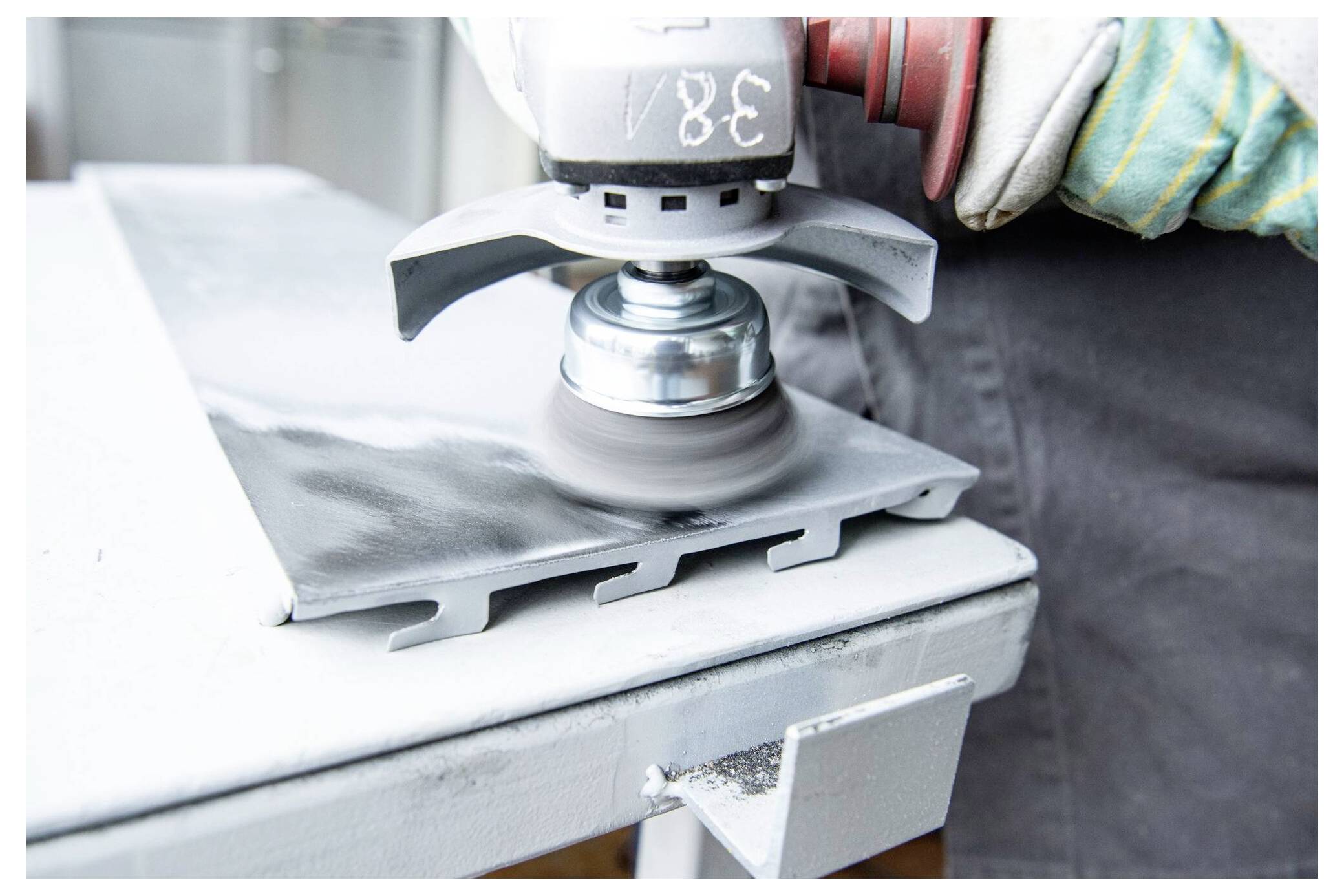 Eine Metalloberfläche, die von einer Person mit Schutzhandschuhen mittels eines Rotationsschleifers poliert wird, mit Betonung auf industrieller Arbeit.