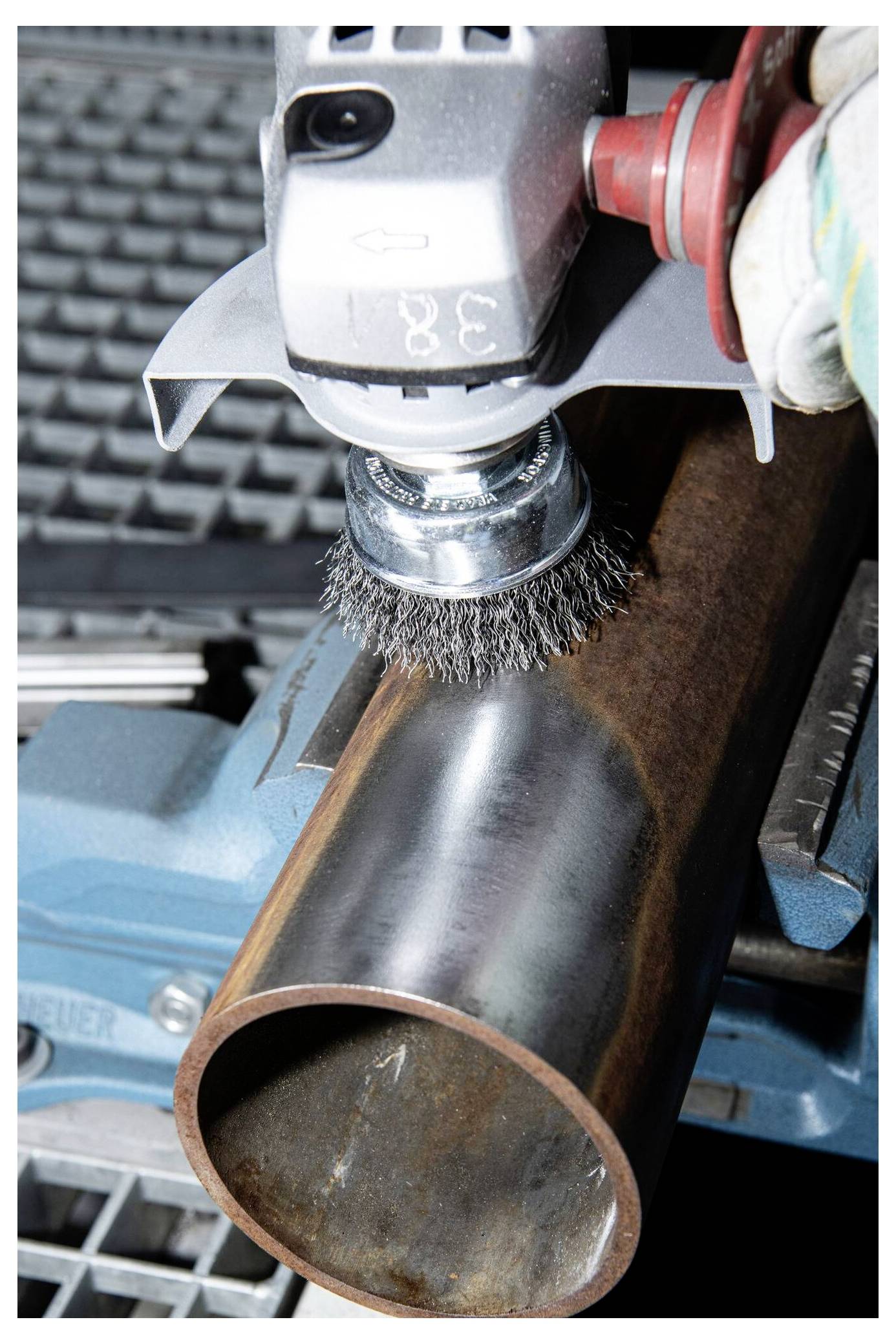 Ein Polierwerkzeug mit einer Drahtbürste glättet die Oberfläche eines Metallrohrs, das auf einer blauen Werkbank liegt.