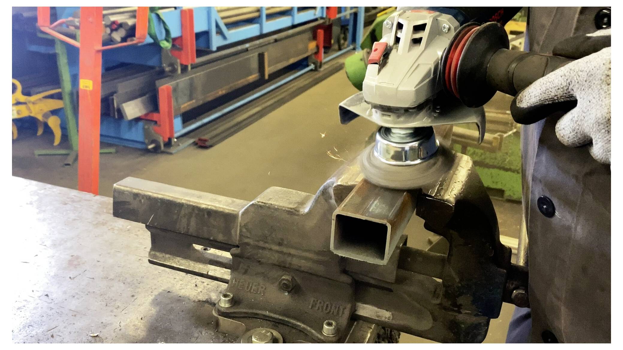 Eine Person verwendet eine Winkelschleifer, um die Kanten eines in einem Schraubstock befestigten Metallrohrs in einer Werkstattumgebung zu glätten.