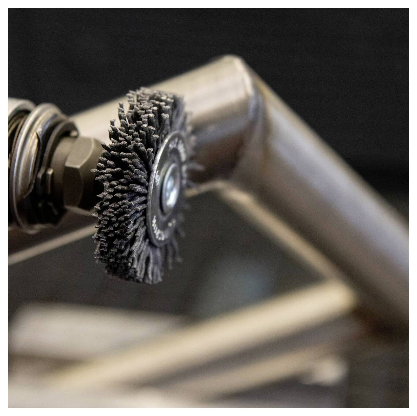 Eine Nahaufnahme einer industriellen Drahtbürste, die an einem Metallrohr befestigt ist und zum Reinigen oder Polieren von Oberflächen verwendet wird, mit einem unscharfen Hintergrund.