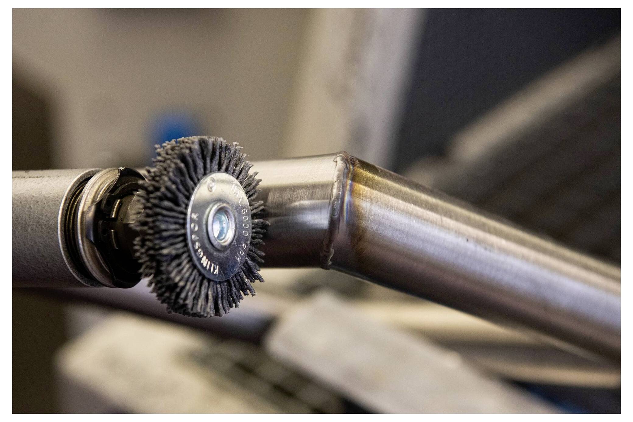 Eine Nahaufnahme eines Drahtbürstenwerkzeugs, das einen Metallrohranschluss poliert und den Prozess des Glättens und Behandelns von Metalloberflächen veranschaulicht.