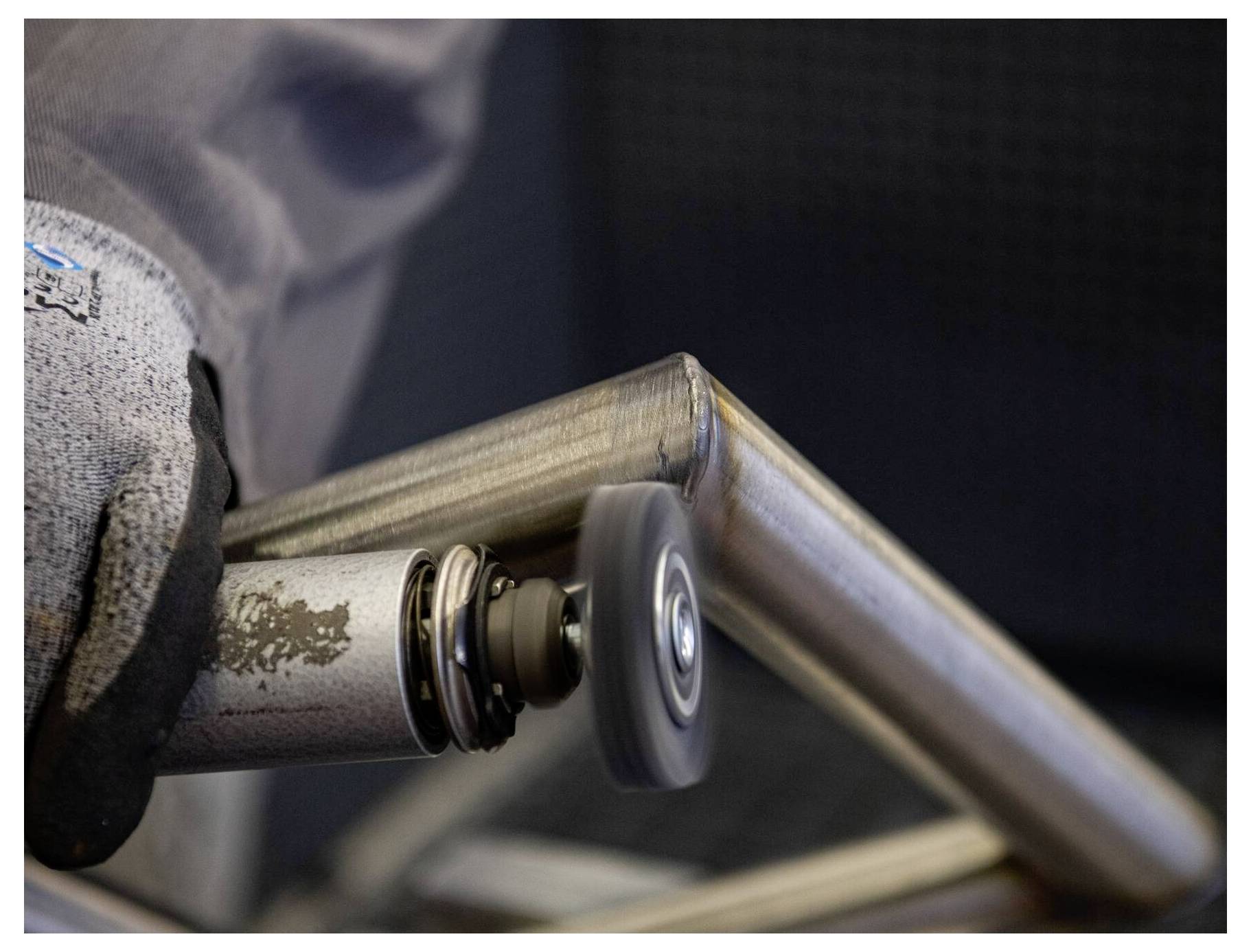 Eine Person mit Handschuh verwendet einen Rotationswerkzeug, um einen Metallrahmen zu polieren und dessen Oberfläche für die Endbearbeitung zu glätten.