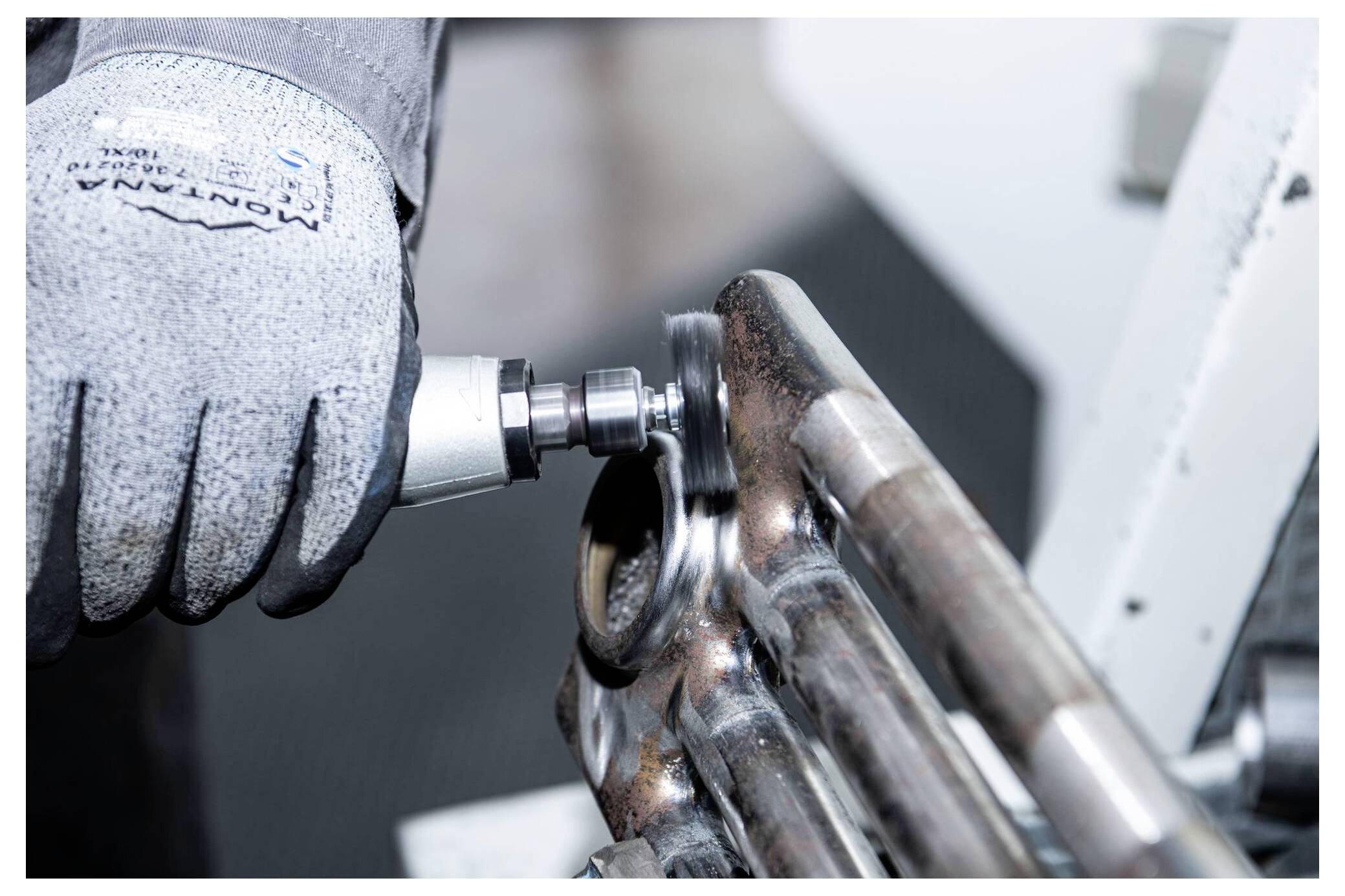 Eine Person trägt einen Handschuh und verwendet ein Rotationswerkzeug, um ein Metallrohr zu polieren, was auf industrielle oder mechanische Arbeit im Gange hindeutet.