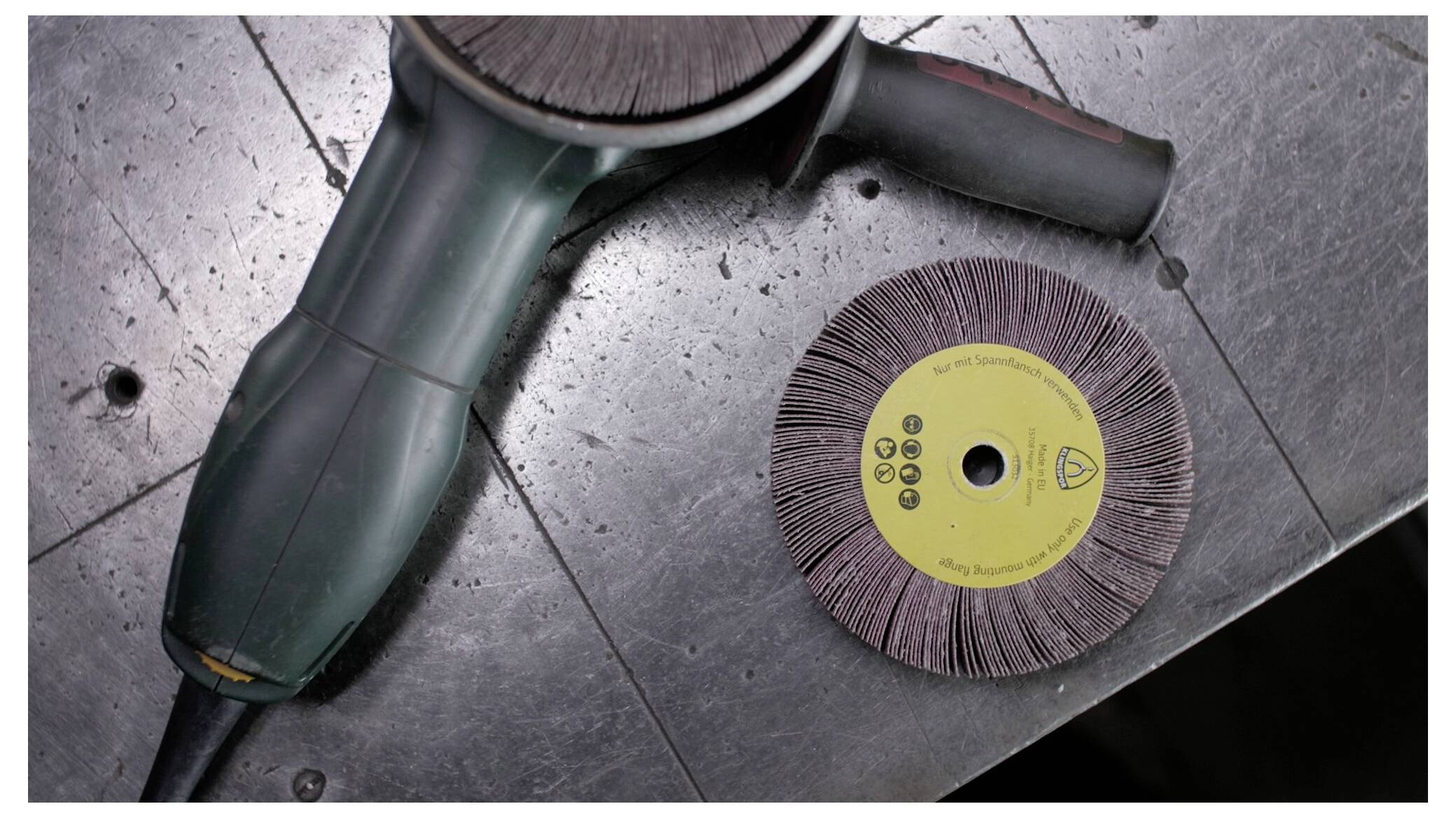 Eine Winkelschleifmaschine und eine kreisförmige Schleifscheibe liegen auf einer Stahloberfläche, Werkzeuge für Metallbearbeitung oder Handwerk.