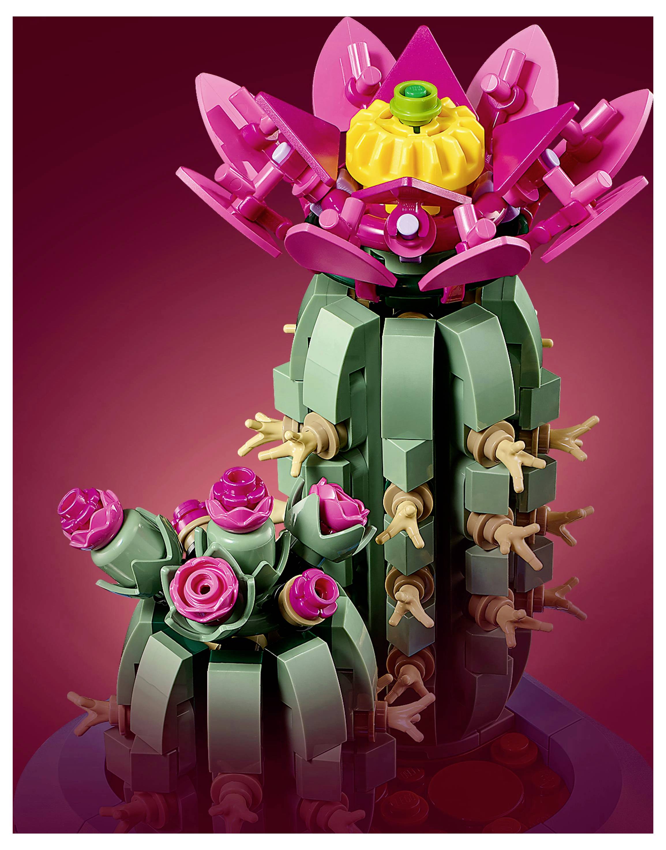 Eine farbenfroh bunte LEGO-Kaktee mit rosa Blüten und grünen Segmenten vor einem Verlaufshintergrund in Rot, die an eine blühende Wüstenpflanze erinnert.
