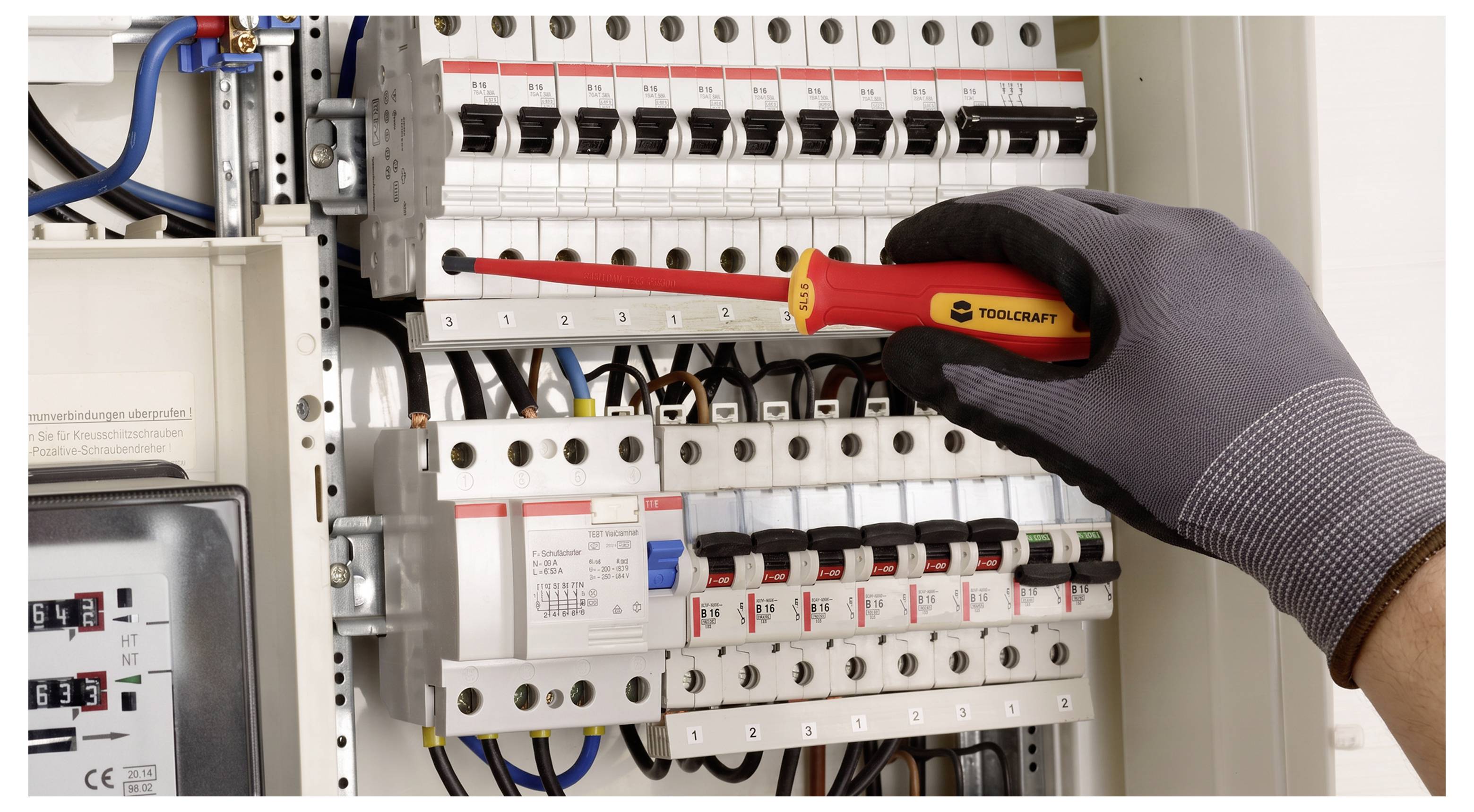 Behandschuhte Hand verwendet einen Schraubenzieher, um einen Leistungsschalter in einem Elektroschrank mit Reihen von Schaltern und Verkabelung festzuziehen.