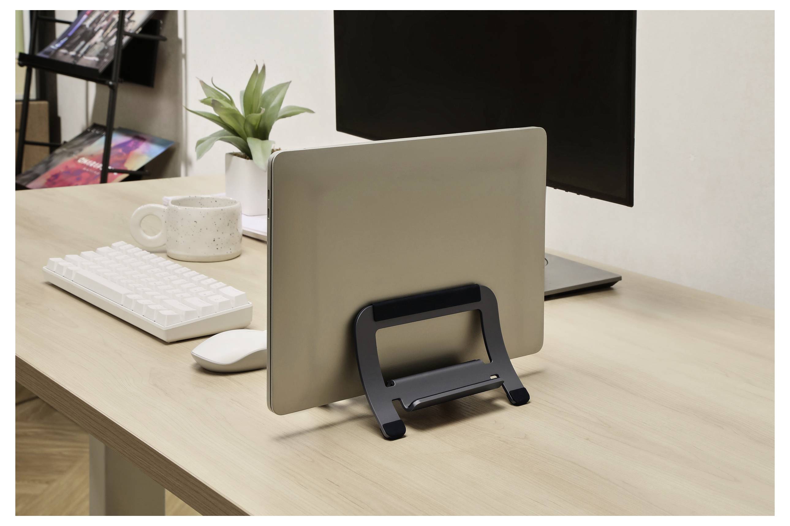Ein Laptop in einem Ständer auf einem Holzschreibtisch mit einer Tastatur, einer Tasse und einer Pflanze, eingerichtet in einer Büroumgebung.