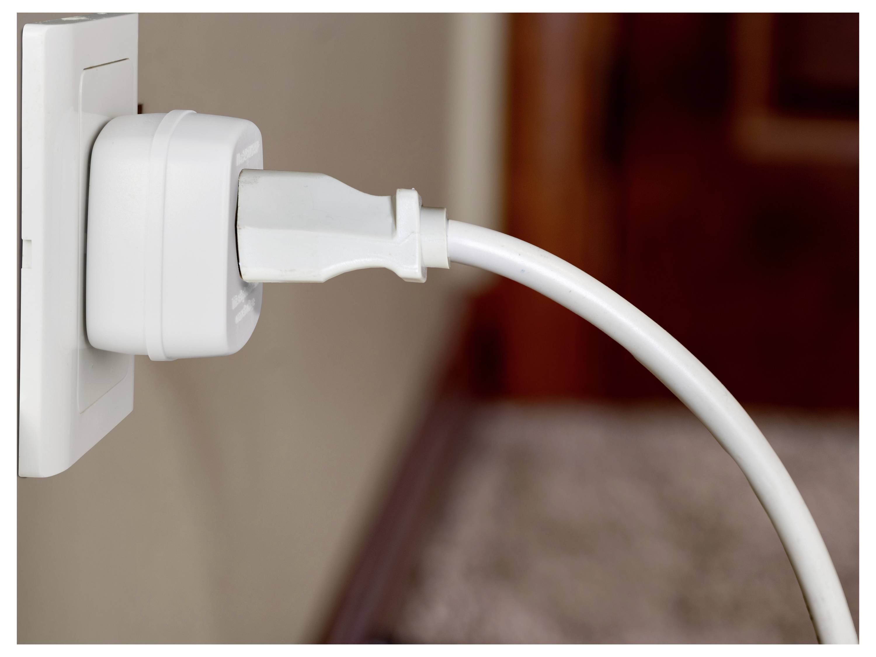 Ein weißer Stecker ist sicher mit einer Steckdose an einer Wand verbunden, wobei sich ein Stromkabel von ihm erstreckt und eine aktive Nutzung andeutet.