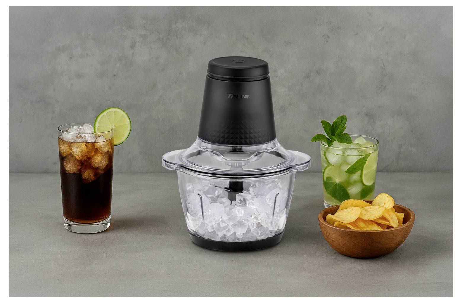 Eine schwarze und durchsichtige Eiscrusher steht in der Mitte, umgeben von einer Cola mit Limette, einem Mojito mit Minze und einer Schüssel Kartoffelchips.