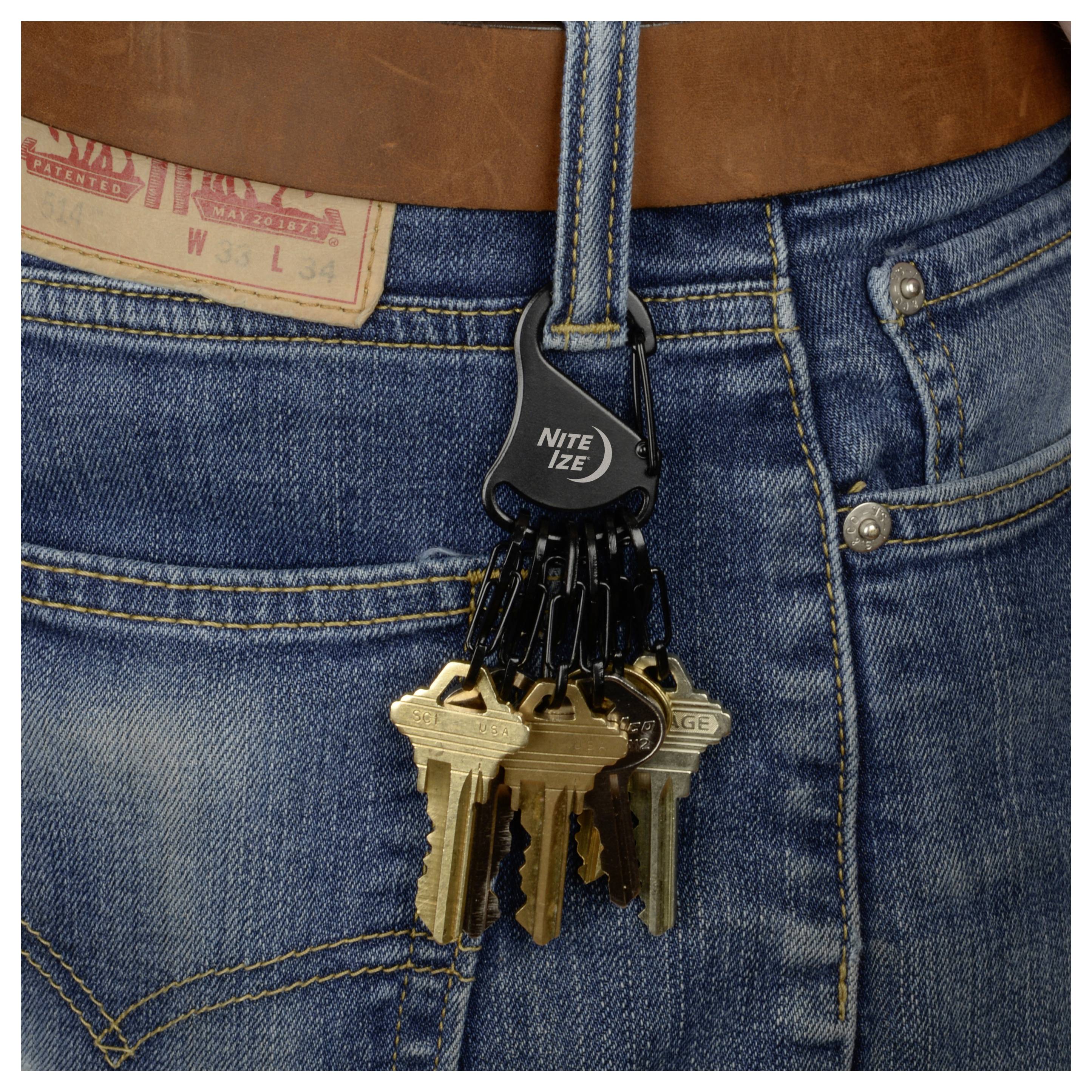 Ein Schlüsselbund, der an einem Nite Ize-Clip befestigt ist, hängt am Gürtelschlaufe einer Person, die blaue Jeans trägt.