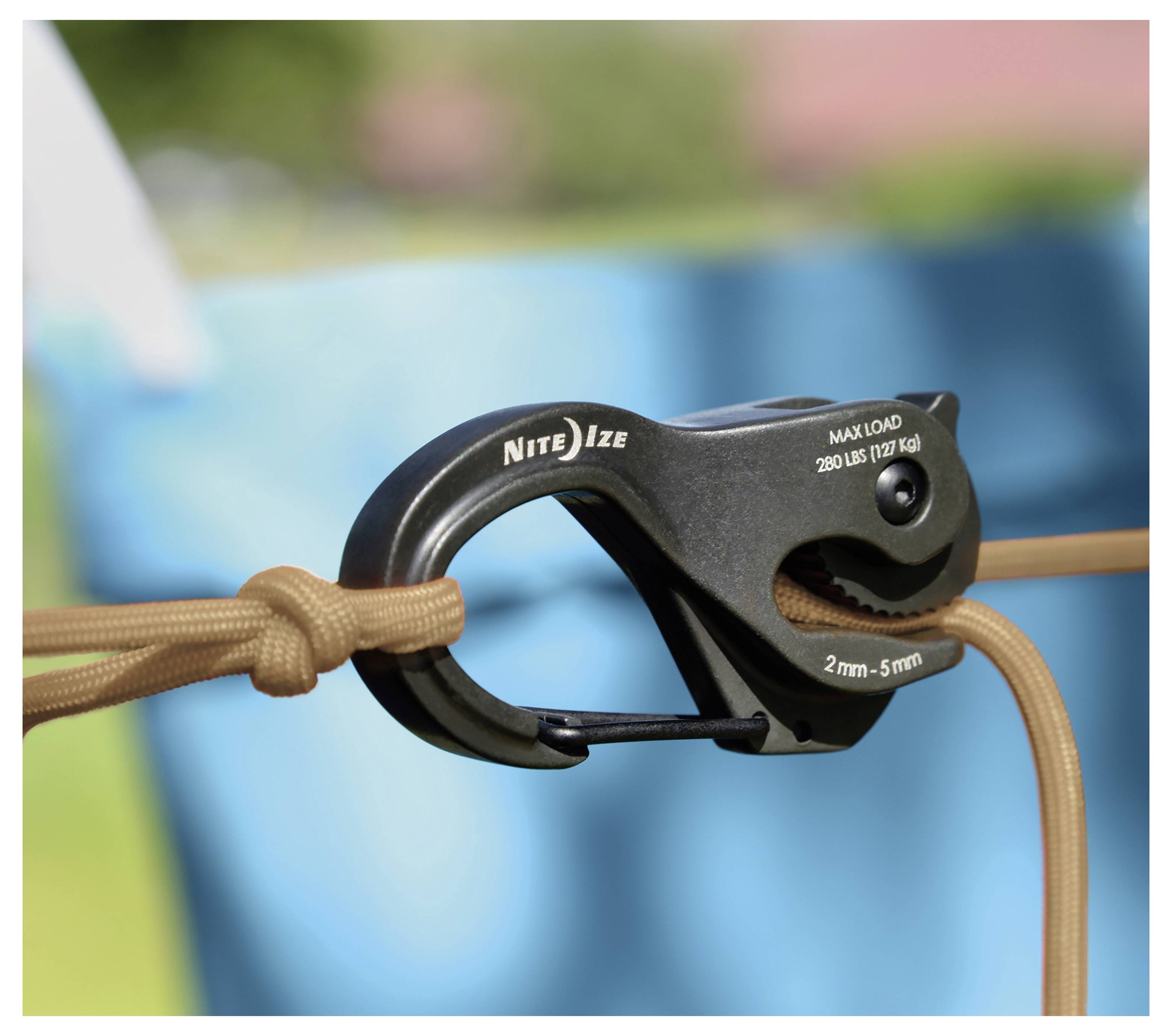 Ein schwarzer Karabinerhaken mit der Aufschrift 'Nite Ize' hält ein braunes Seil, mit Text, der eine maximale Belastung von 280 lbs (127 kg) und eine Größe von 2mm-5mm angibt.