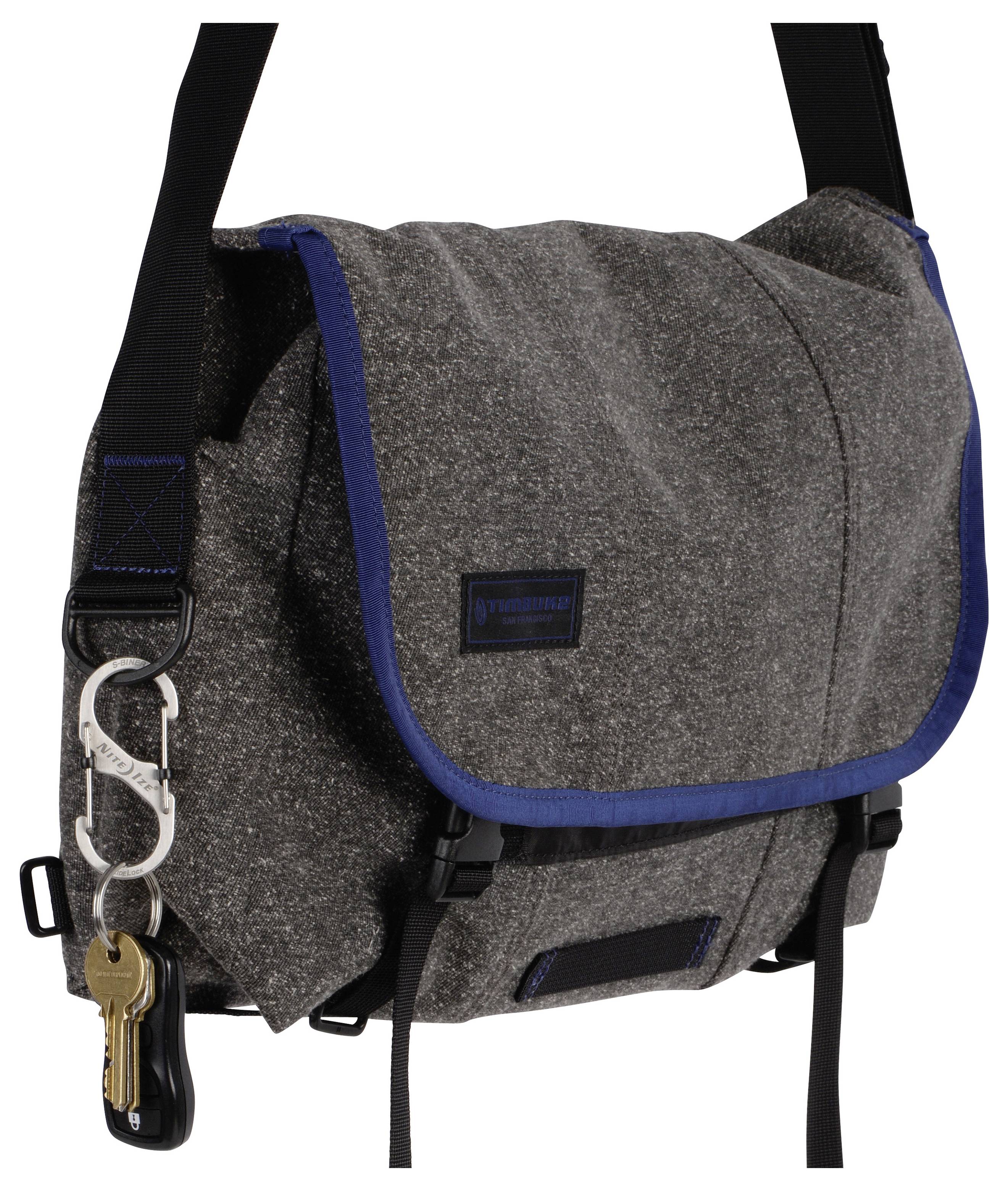 Eine graue und blaue Umhängetasche mit Klappe und verstellbarem Riemen. Ein Karabiner mit Schlüsseln ist zur Bequemlichkeit am Riemen befestigt.