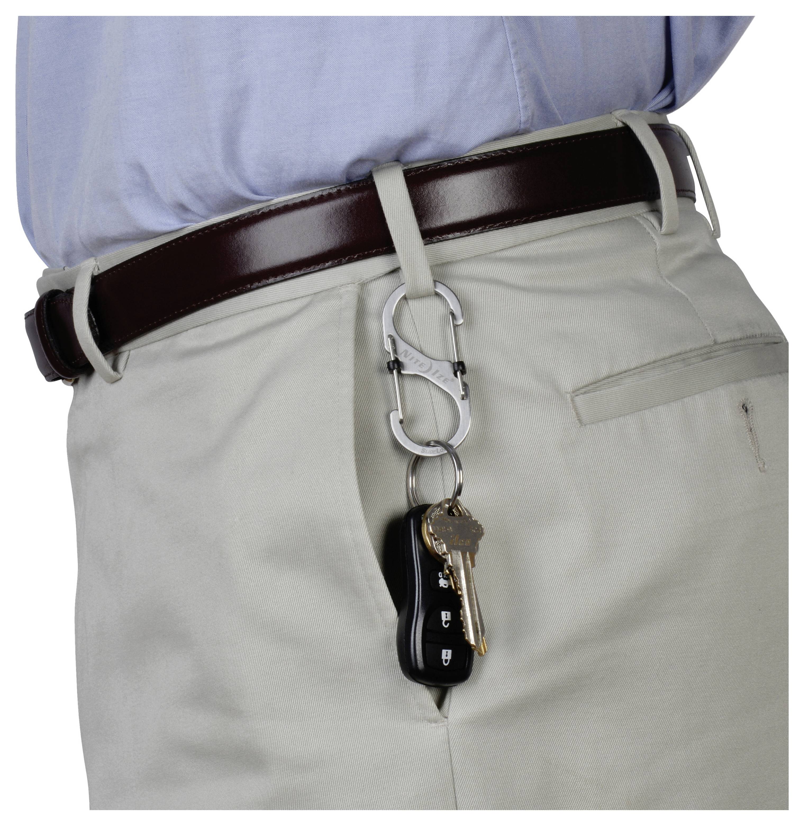 Eine Person trägt beige Hosen und einen braunen Gürtel und hält Schlüssel an einem silbernen Karabiner, der an einer Gürtelschlaufe befestigt ist, was einen schlüssellosen Ansatz unterstreicht.