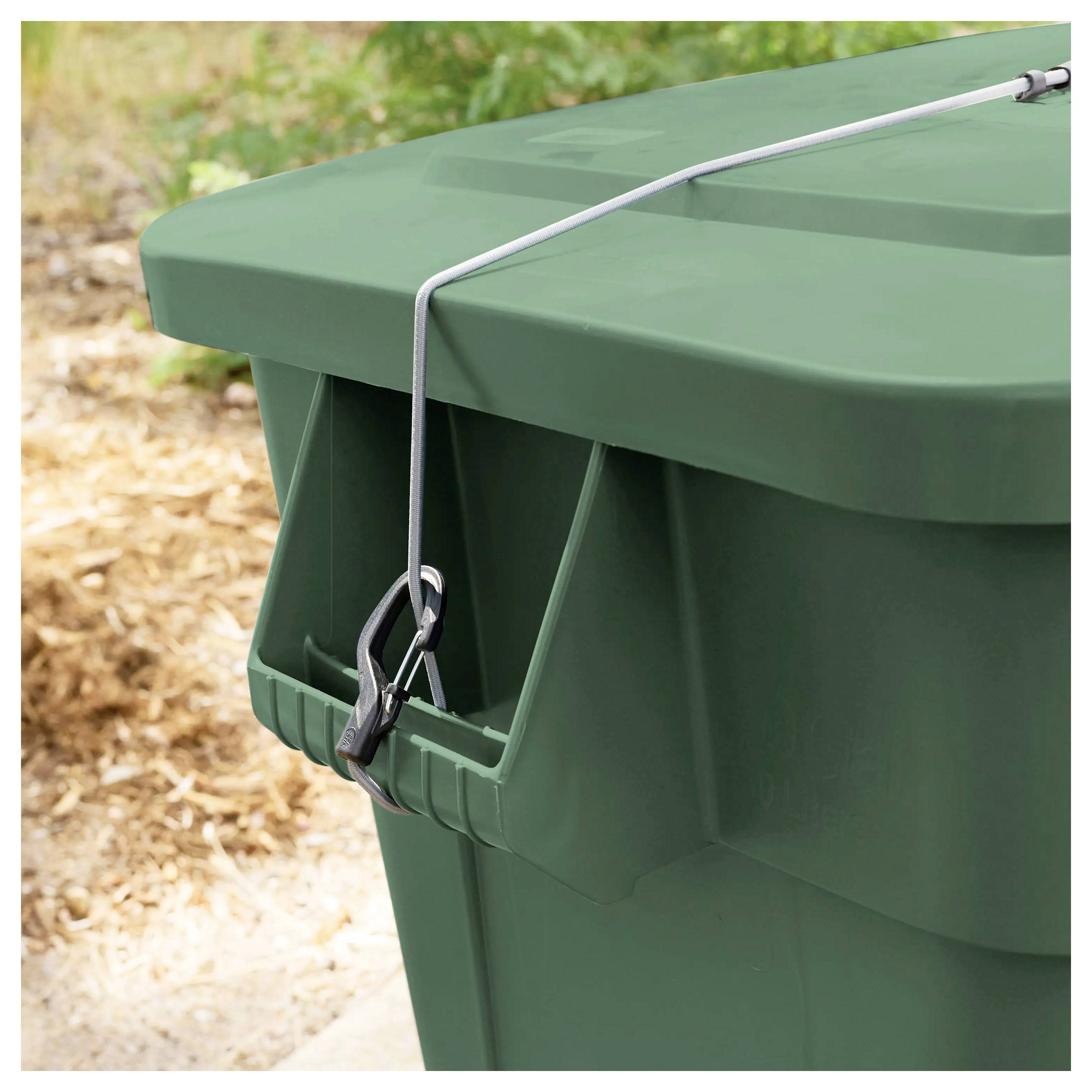 Eine grüne Outdoor-Mülltonne mit einem sicheren Verschlusskabel über dem Deckel, die auf einer Betonfläche mit trockenen Blättern im Hintergrund steht.